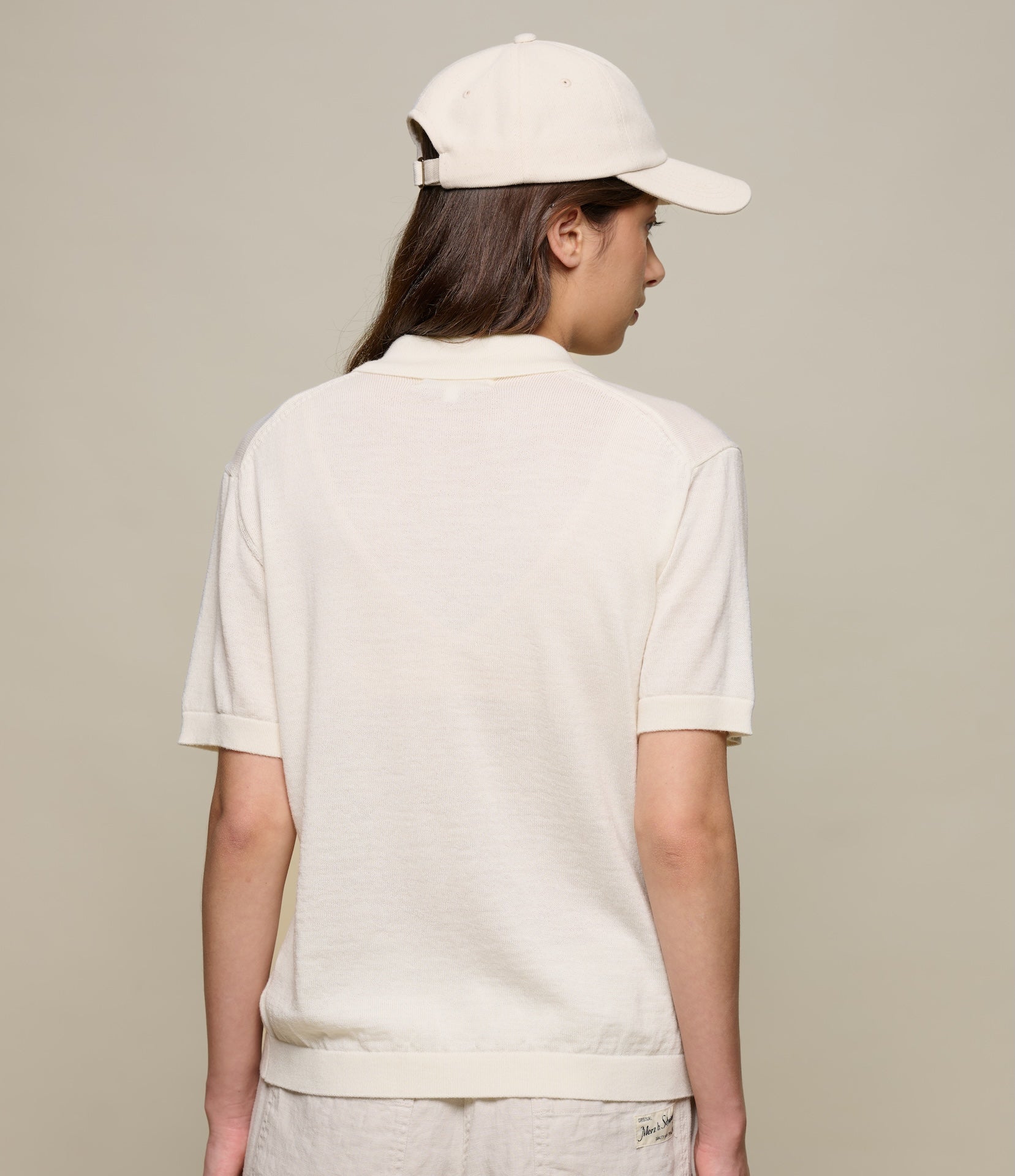 Person wearing a beige knitted polo shirt and cap on a beige background