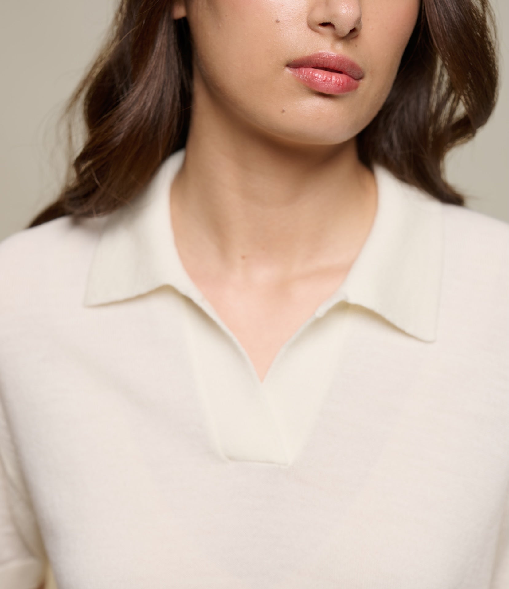 Close-up of a person wearing a beige knitted polo shirt with a collar.