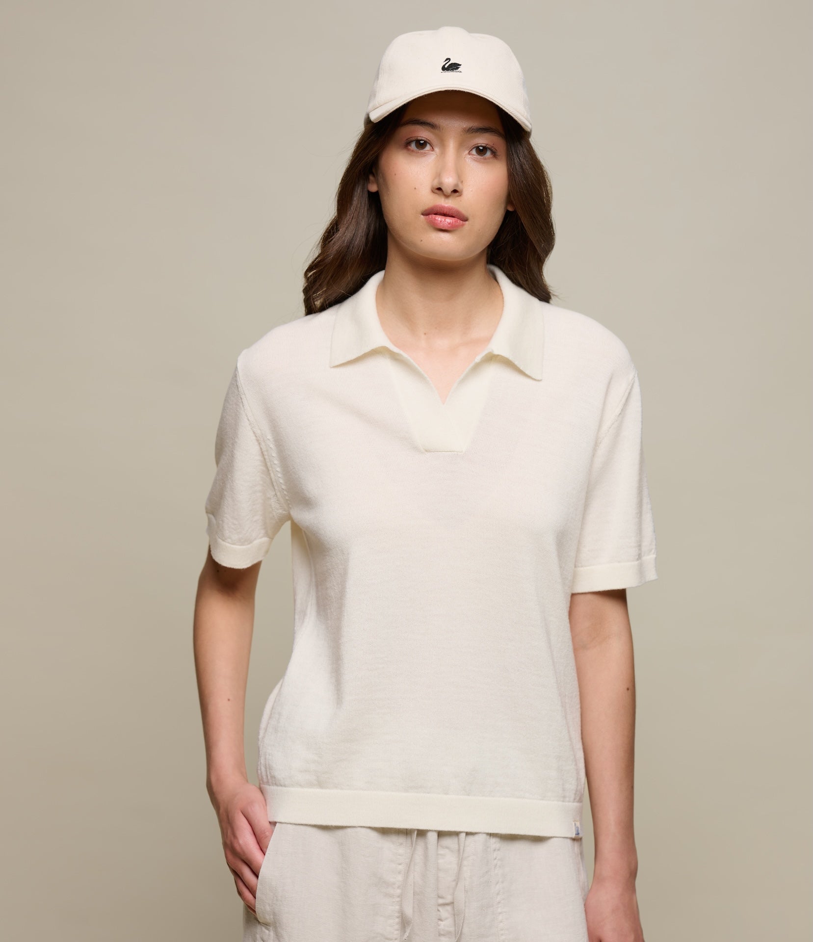Person wearing a beige knited polo shirt and cap against a plain background