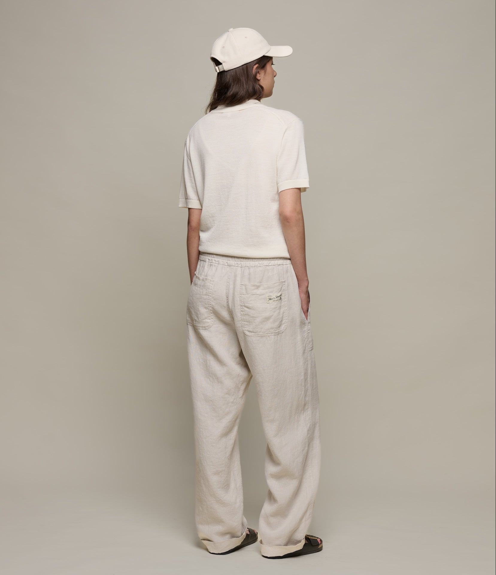 Person wearing a beige polo shirt and beige pants with a cap, standing against a plain background