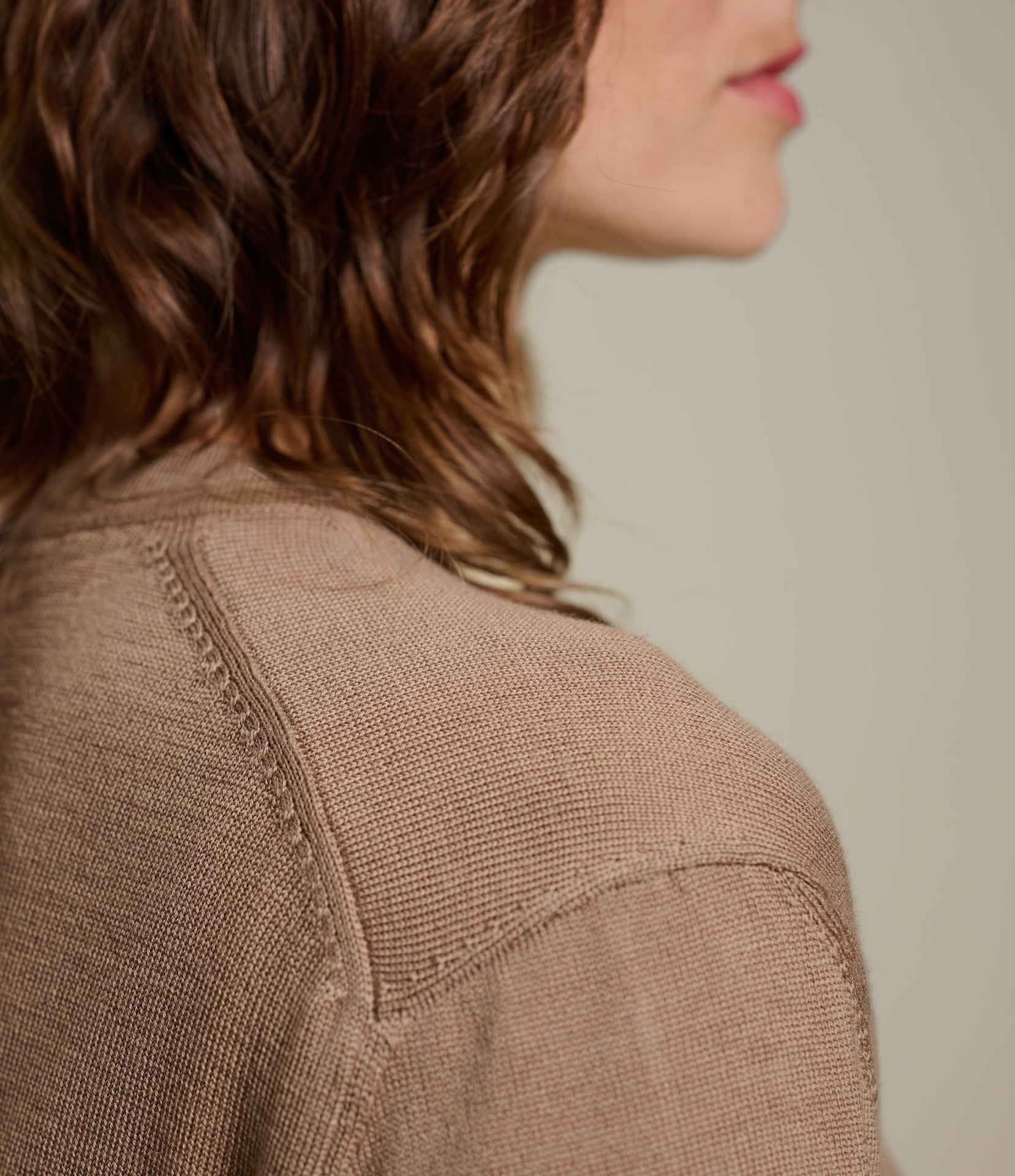 Close-up of a person wearing a brown knitted T-shirt against a neutral background
