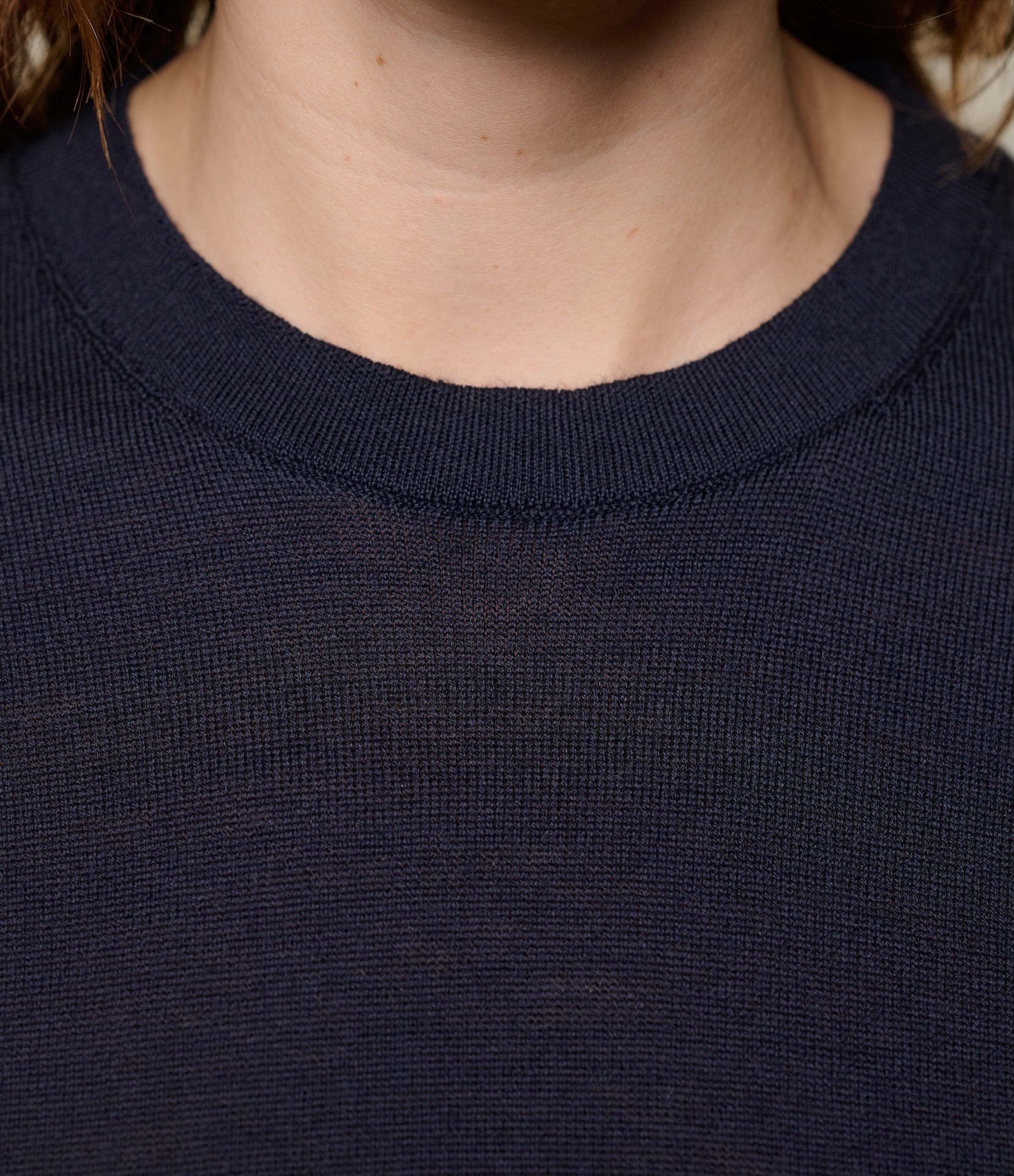 Close-up of a person wearing a dark blue knitted T-shirt with a focus on the neckline.