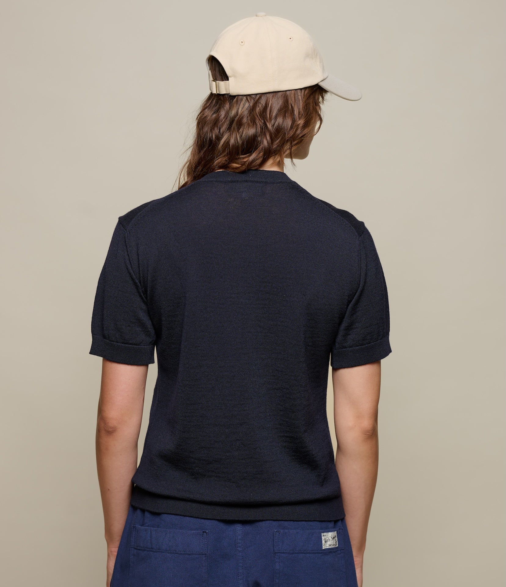 Person wearing a navy blue knitted polo shirt and beige cap on a beige background