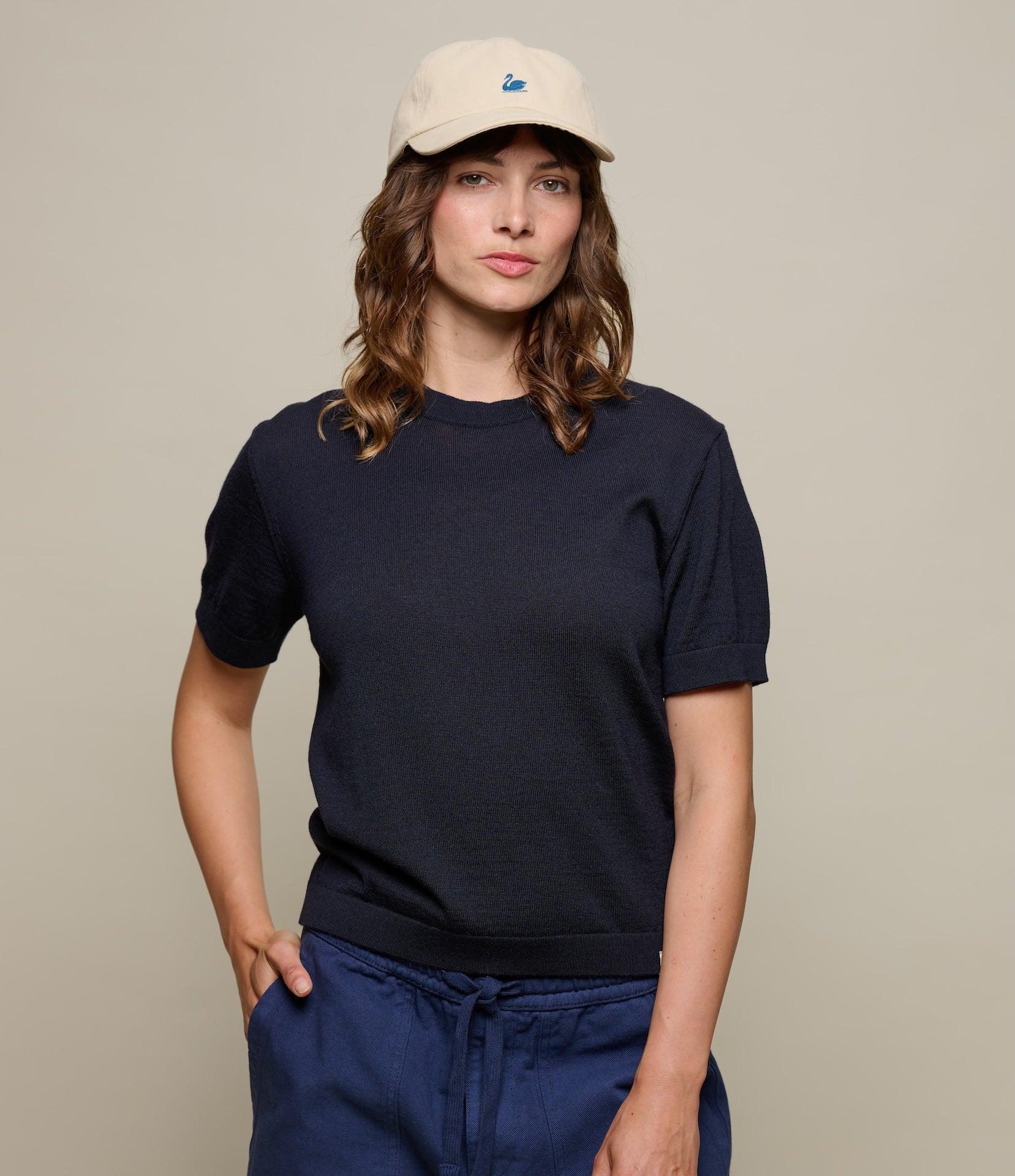 Woman wearing a knitted navy blue t-shirt and beige cap against a plain background