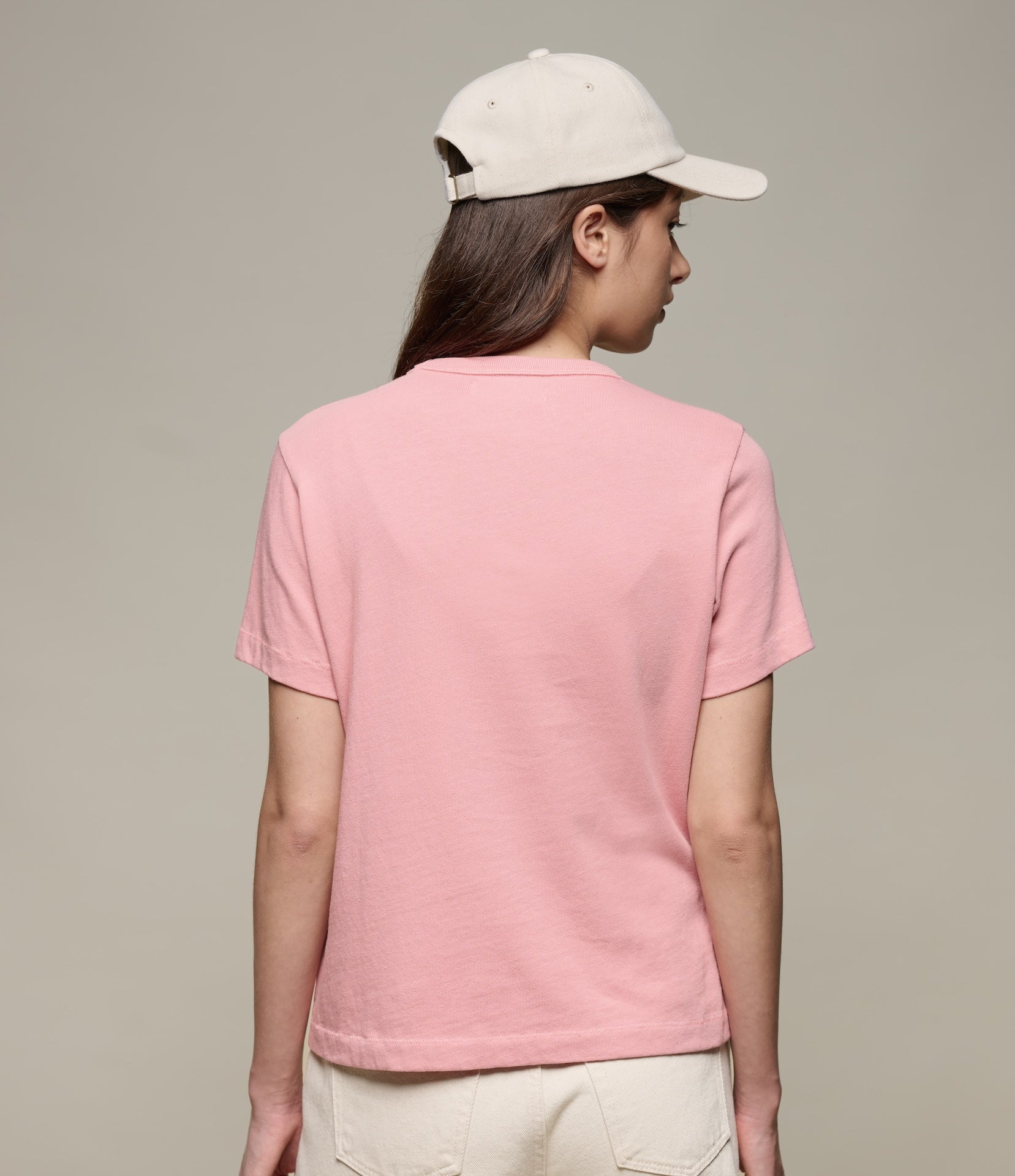 Person wearing a pink t-shirt and beige cap on a plain background