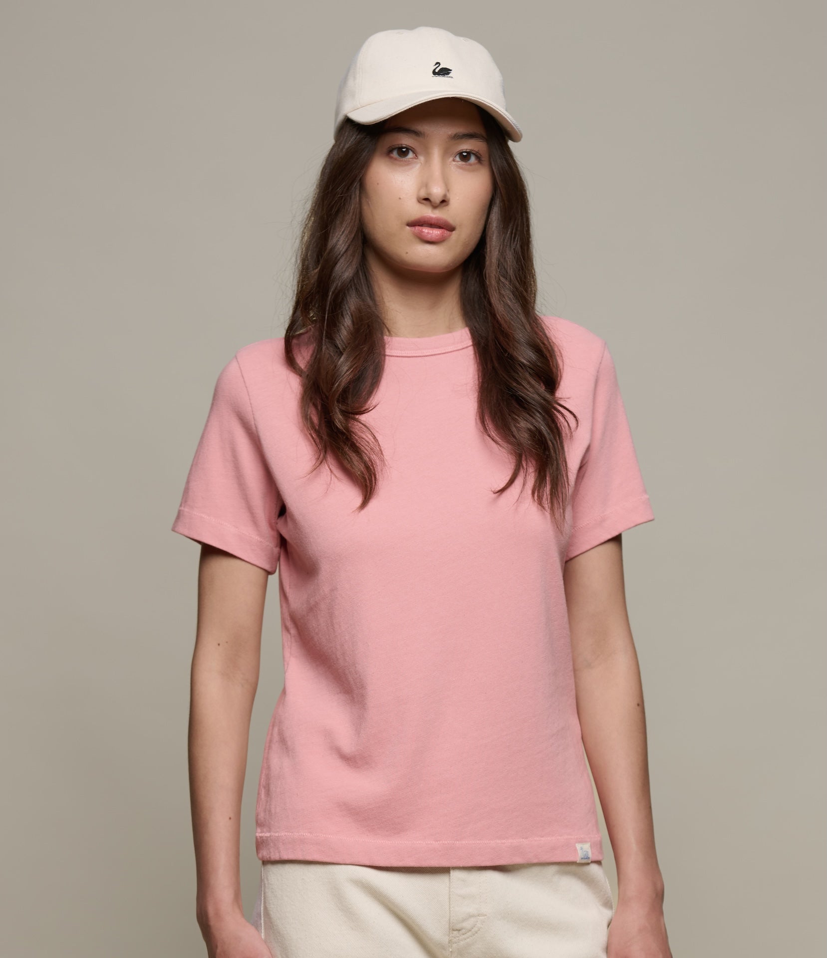 Person wearing a pink authentic jersey t-shirt and beige cap on a plain background