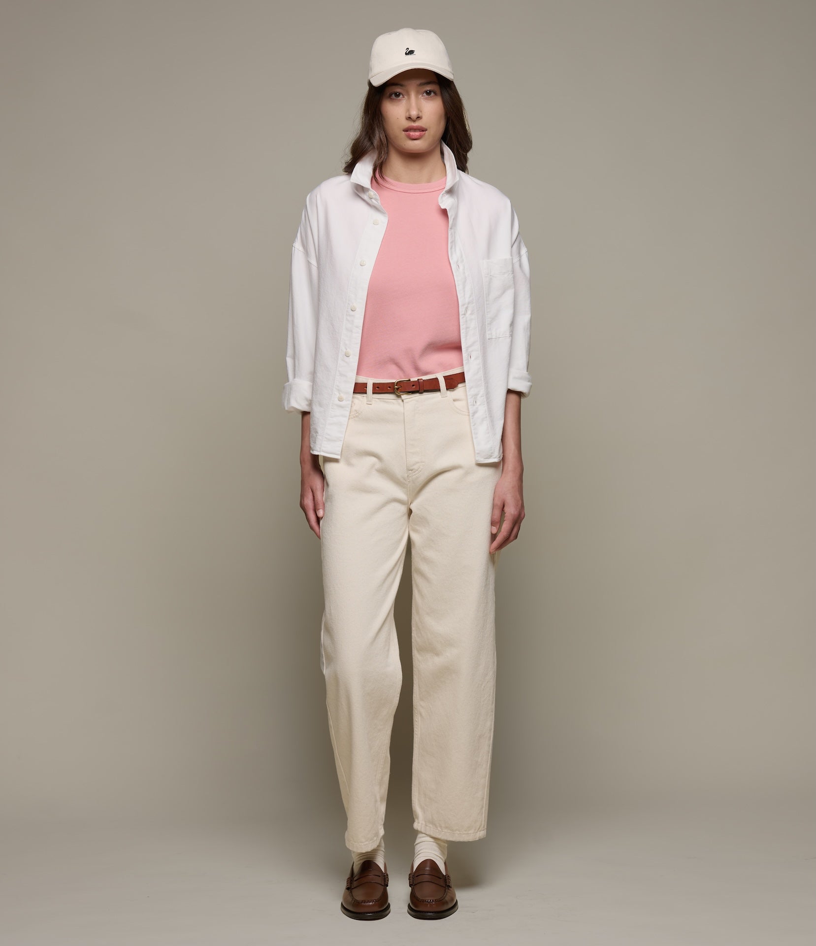 Person wearing a white shirt, pink t-shirt, beige pants, and brown shoes against a plain background