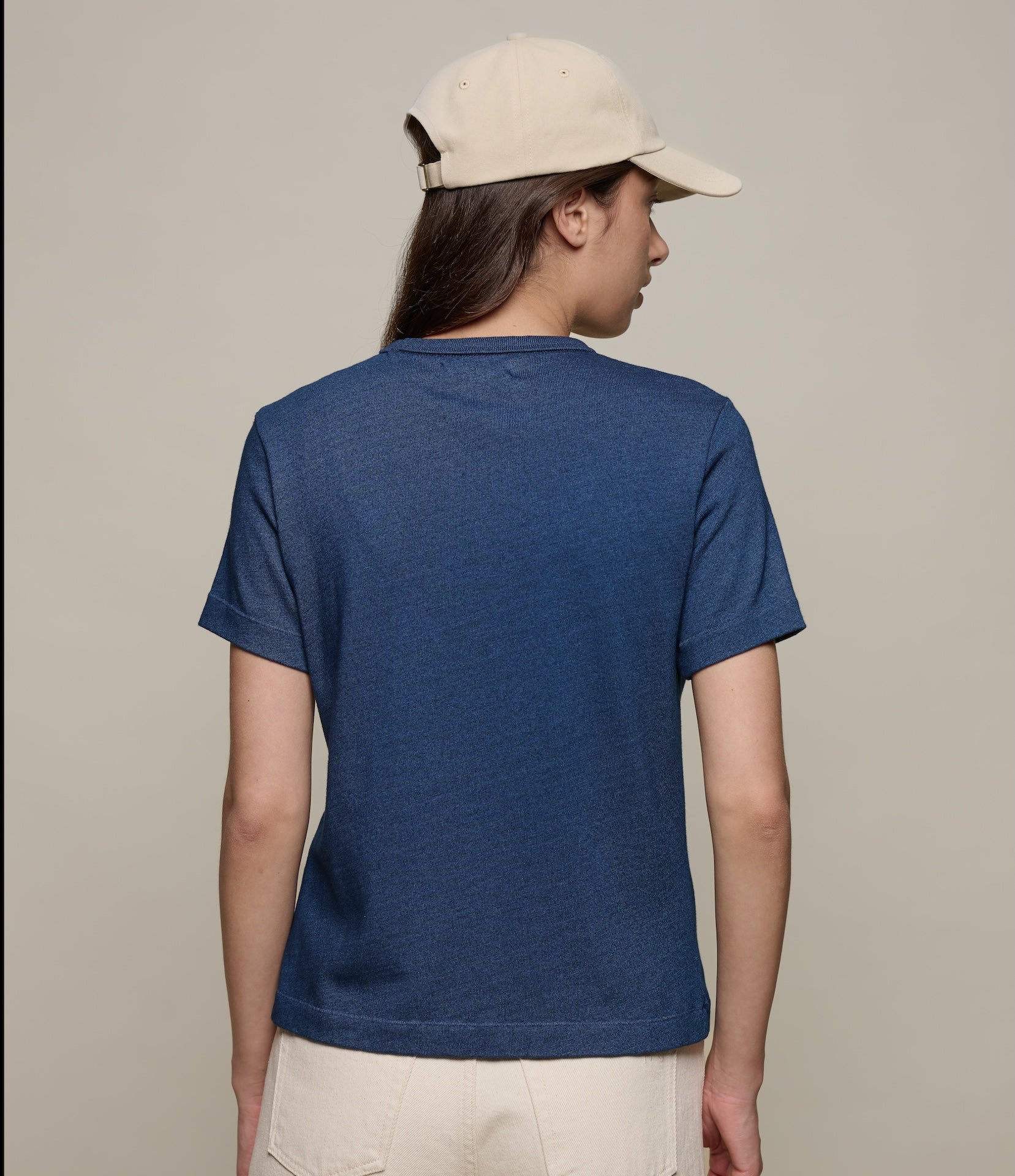 Person wearing an indigo blue organic cotton t-shirt and beige cap on a plain background