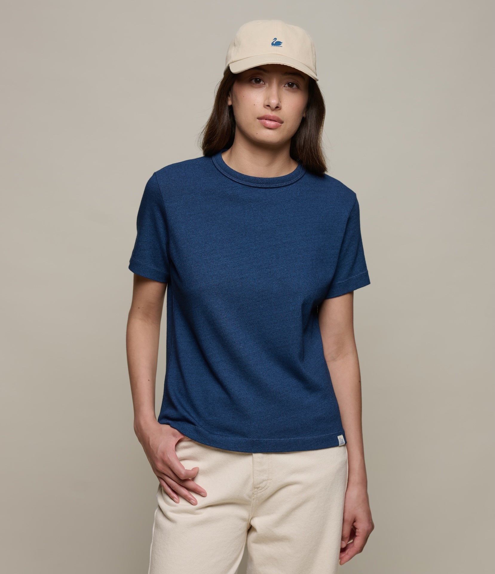 Person wearing an indigo blue authentic jersey t-shirt and beige cap on a plain background