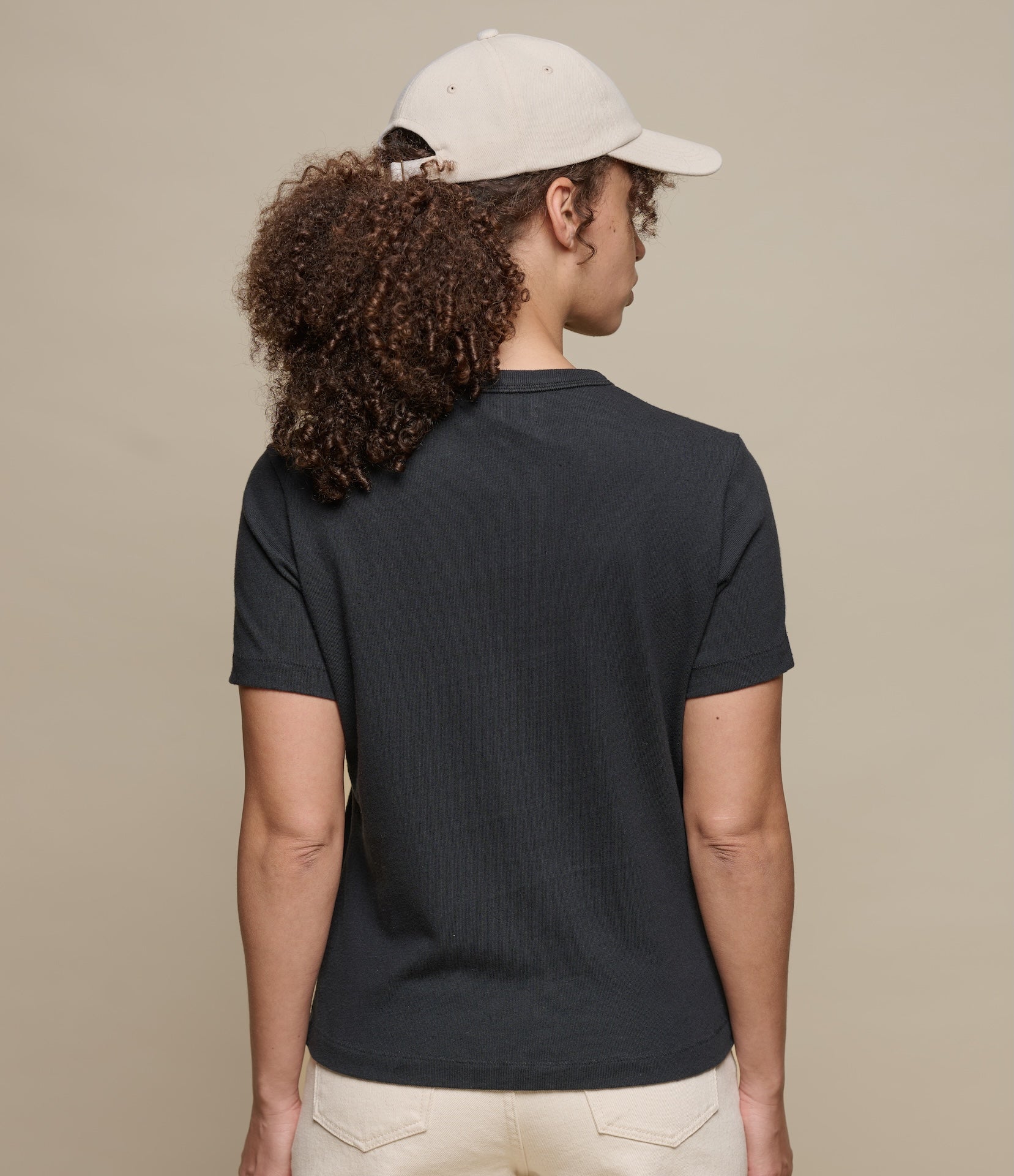 Person wearing a black t-shirt and white cap from behind on a beige background