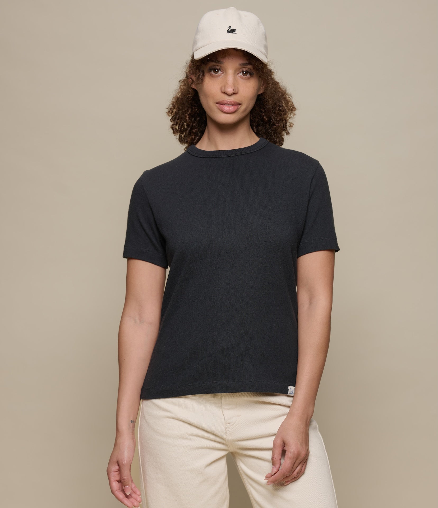 Person wearing a black authentic jersey t-shirt and beige cap on a beige background