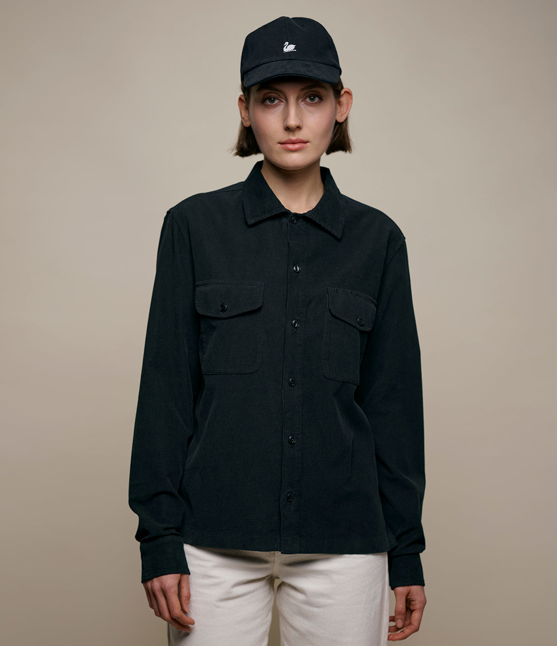 Person wearing a black corduroy shirt and cap against a beige background