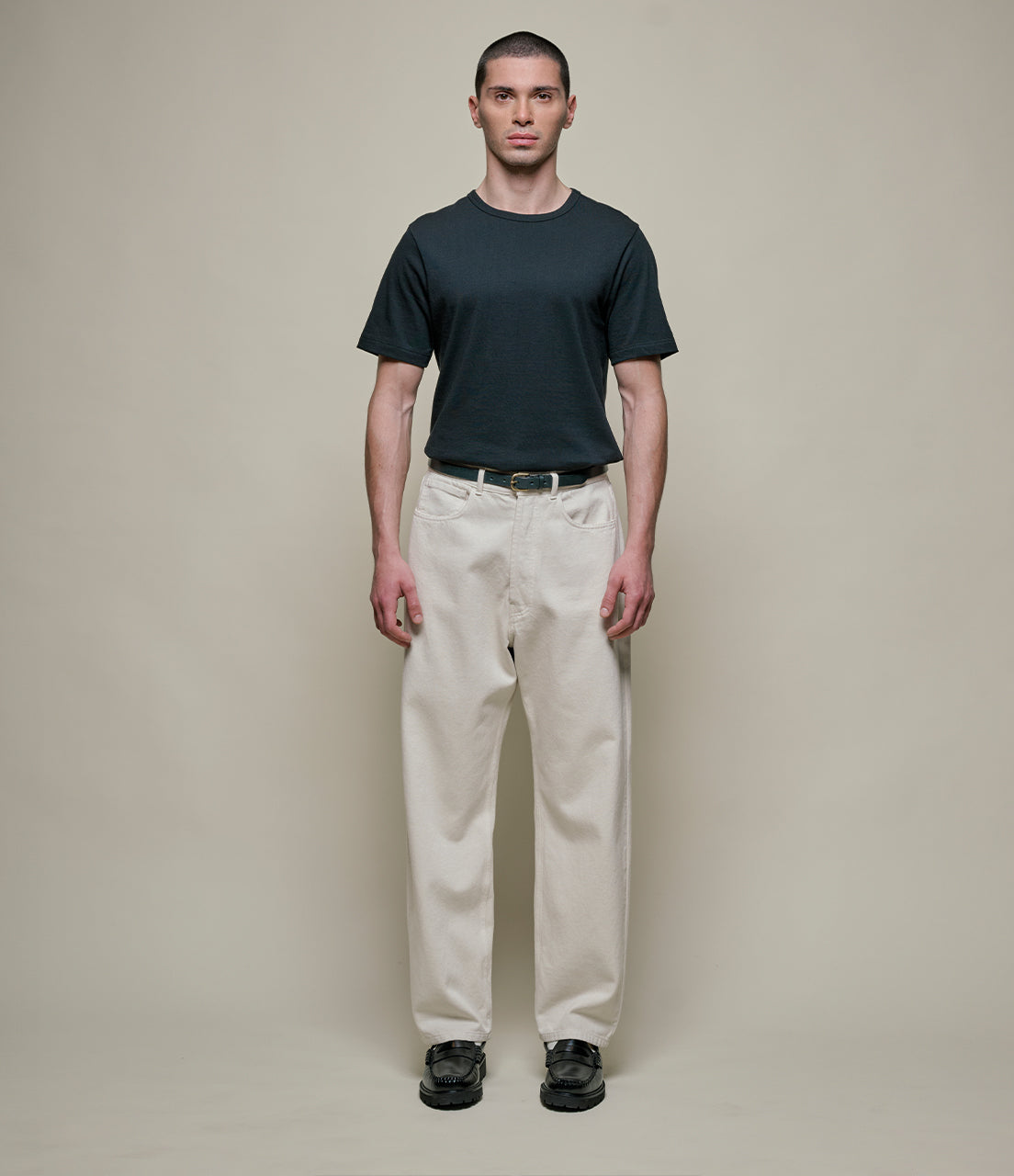 Man wearing a black t-shirt and beige pants against a plain background