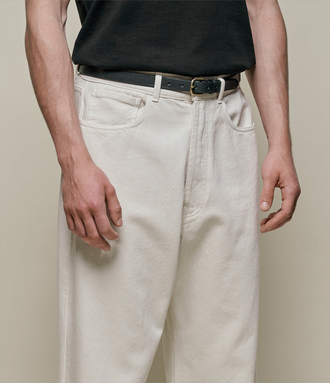 Person wearing light-colored pants and a black shirt on a beige background