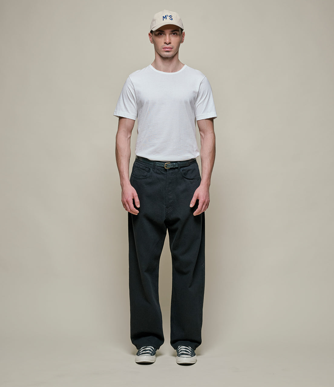 Man wearing a white t-shirt, black pants, and a cap on a plain background