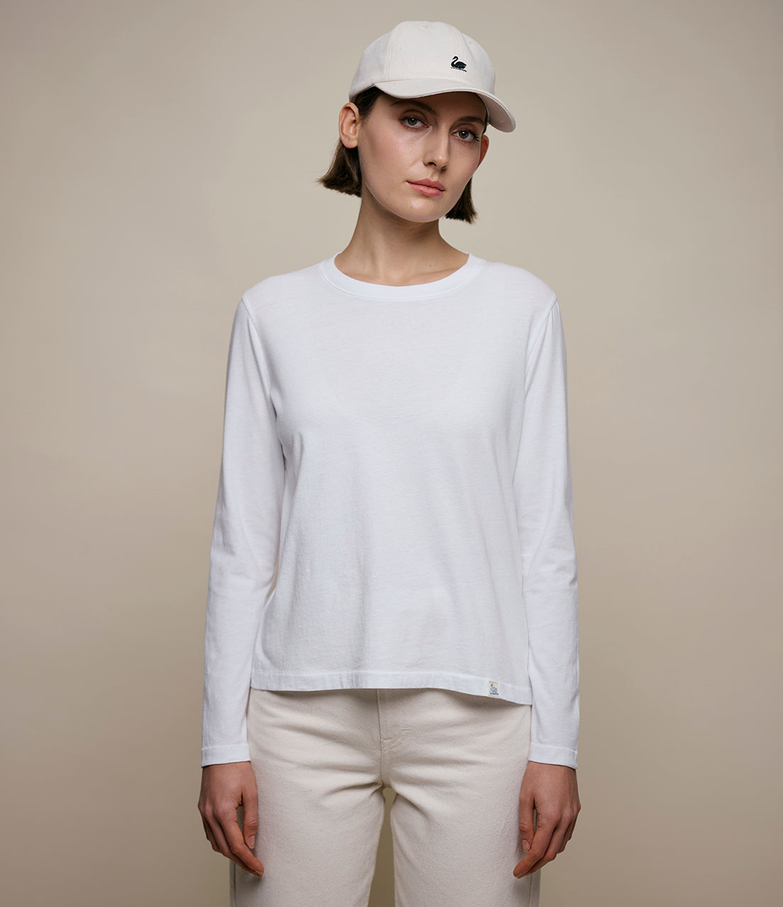 Person wearing a white long-sleeve shirt and cap against a beige background
