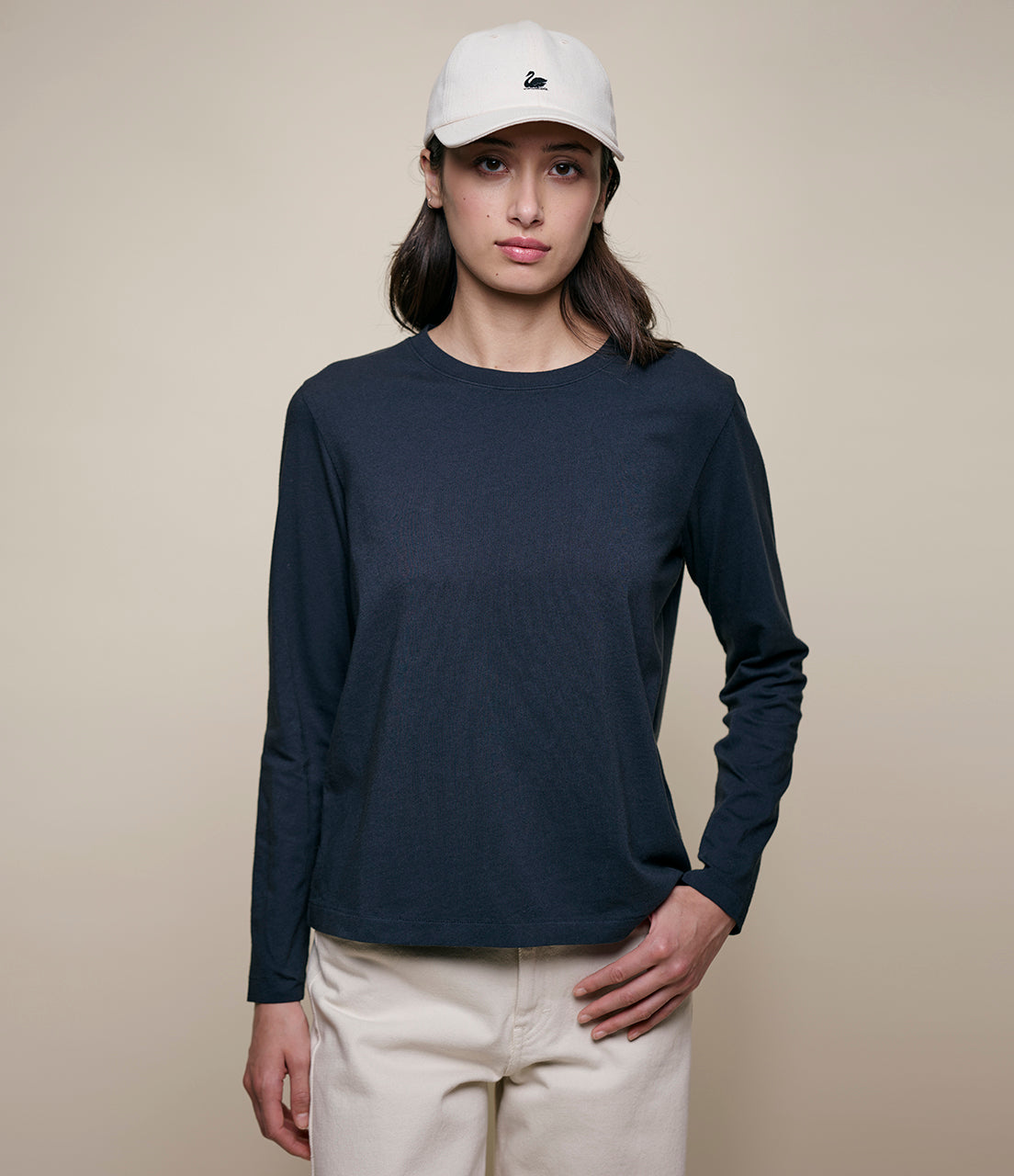 Person wearing a navy long-sleeve shirt, beige pants, and a white cap on a beige background