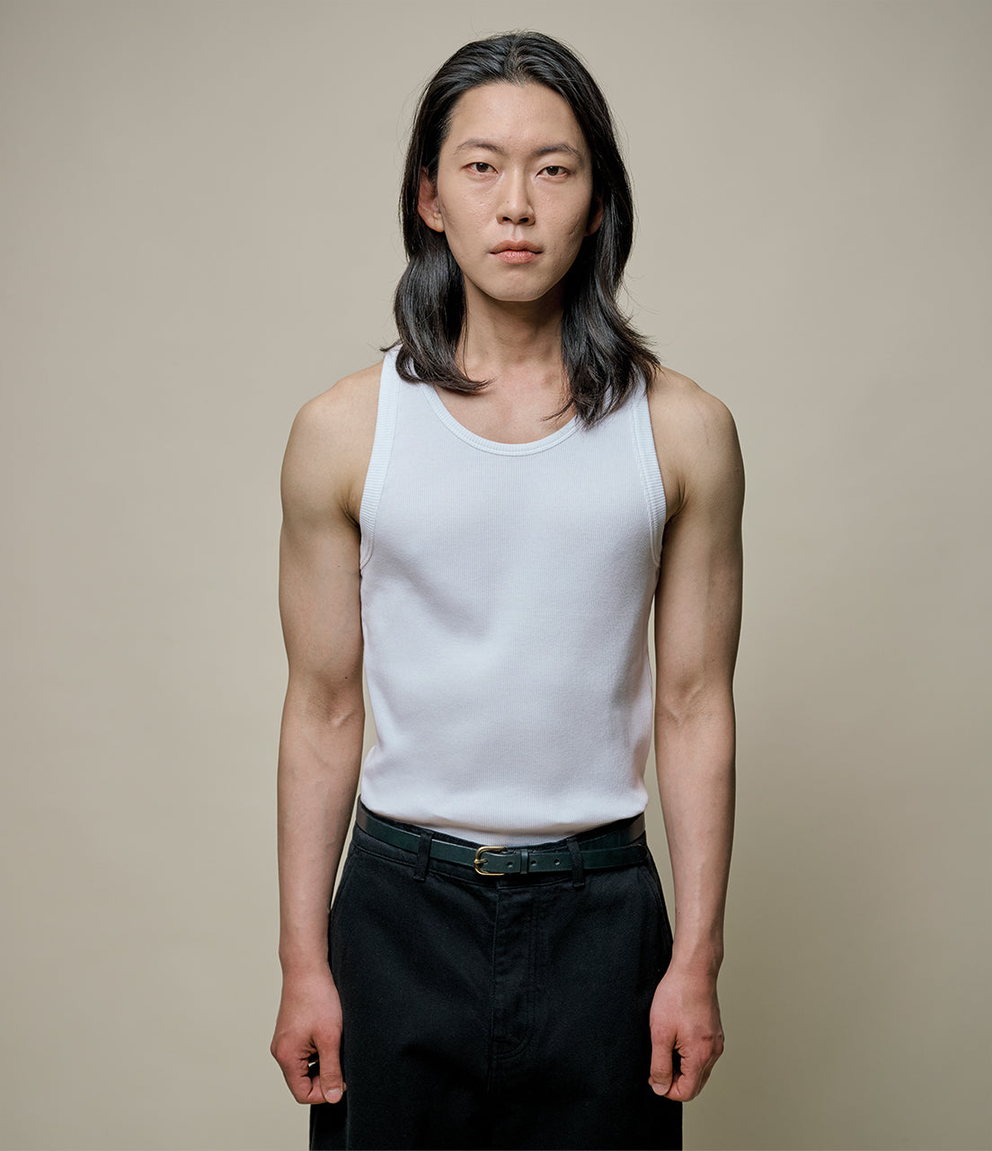 Man wearing a white tank top and black pants against a plain background