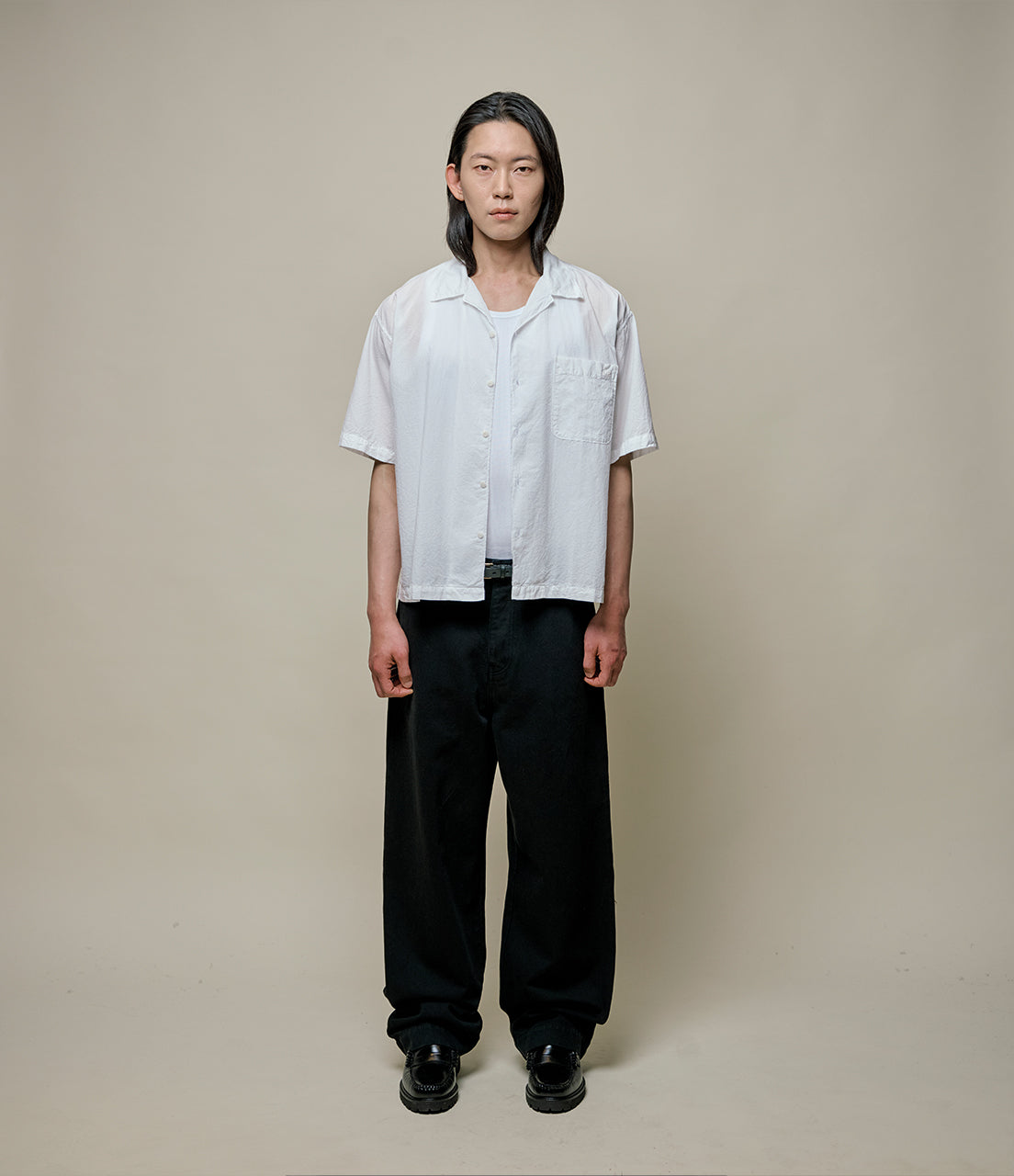 Person wearing a white shirt and black pants against a plain background