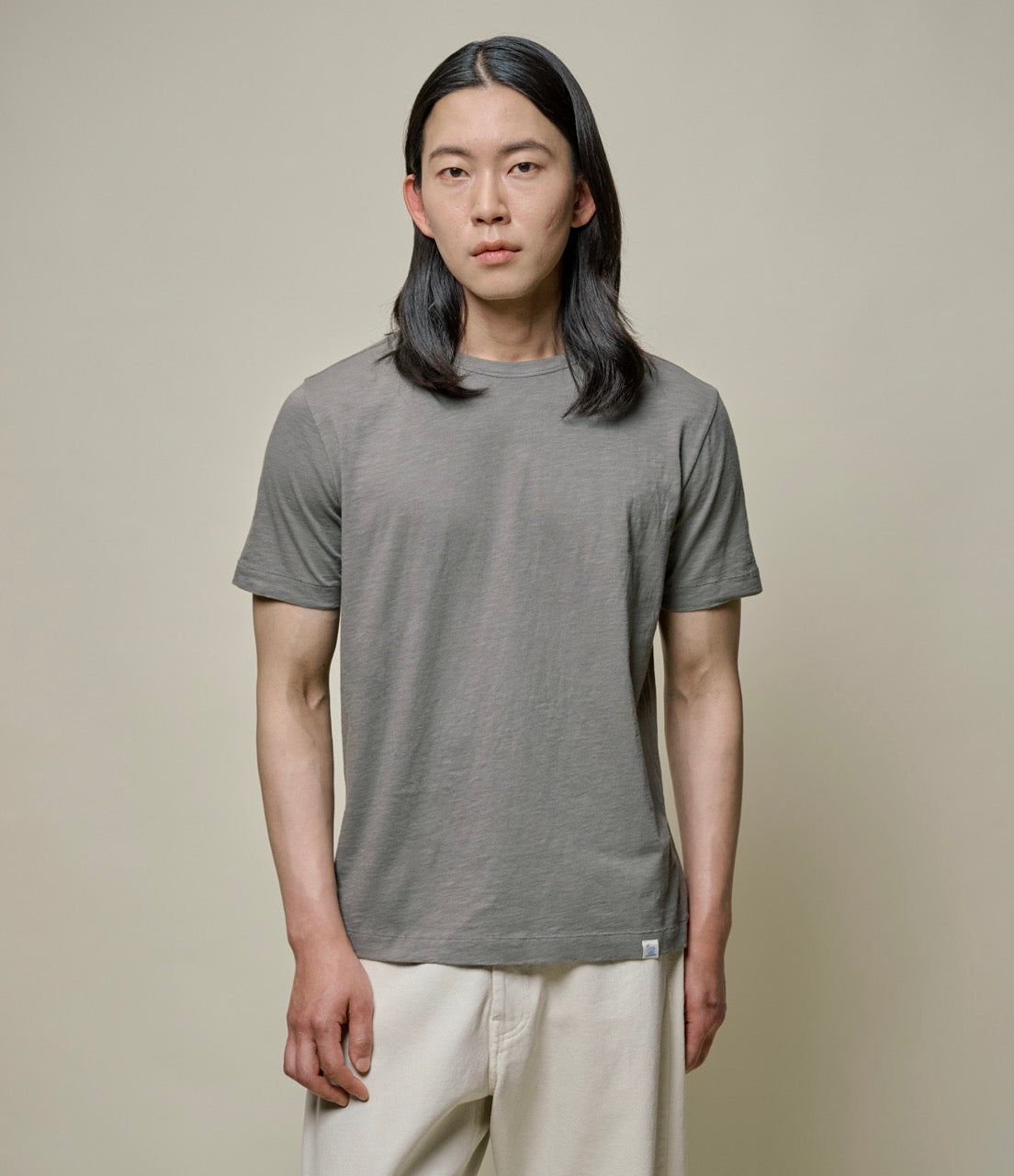 A person wearing a green short-sleeved crew neck T-shirt and light-colored pants.