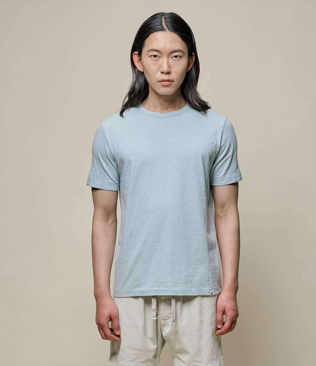Person wearing a light blue t-shirt and beige pants against a plain background