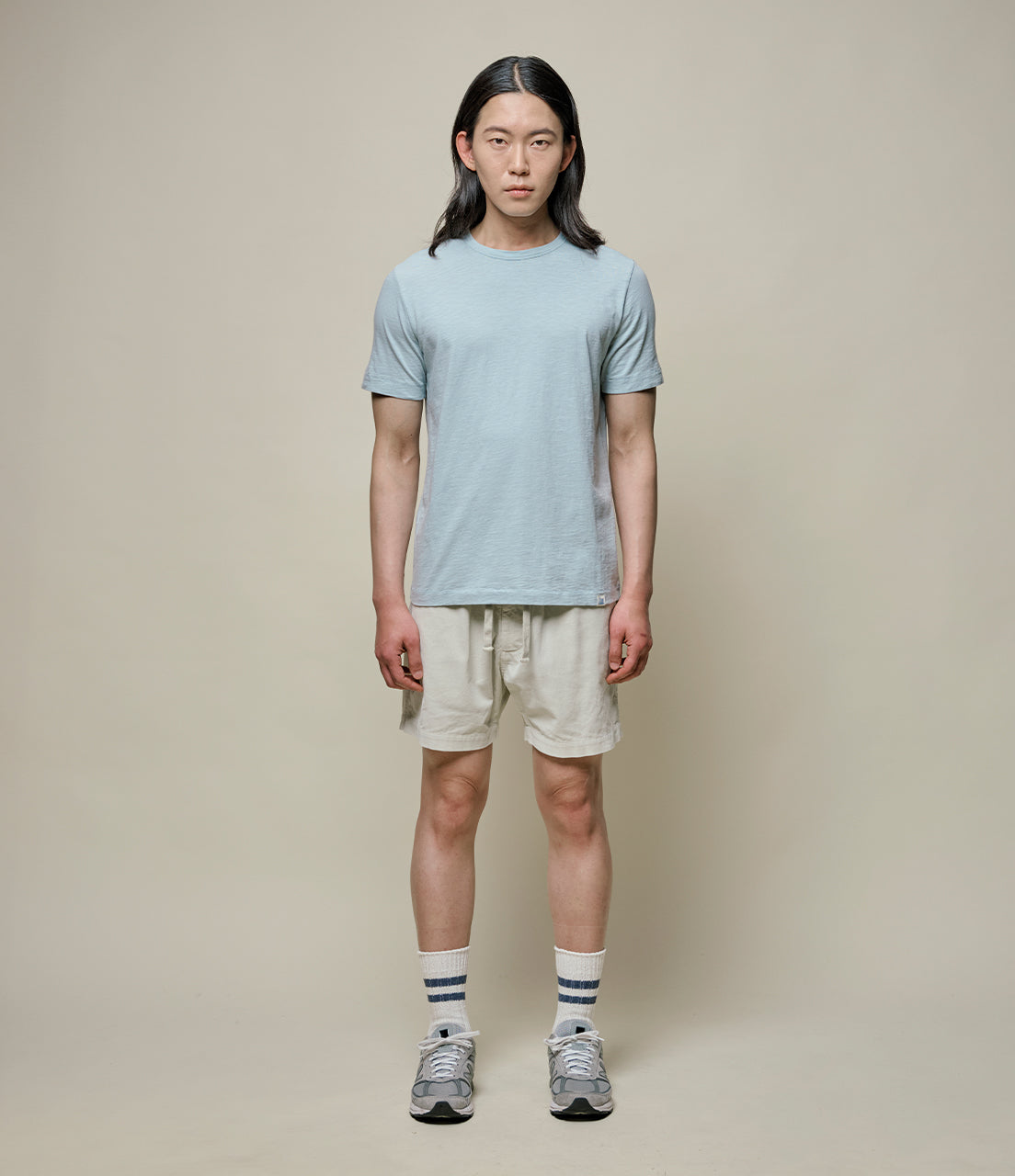 Person wearing a light blue t-shirt and beige shorts on a plain background