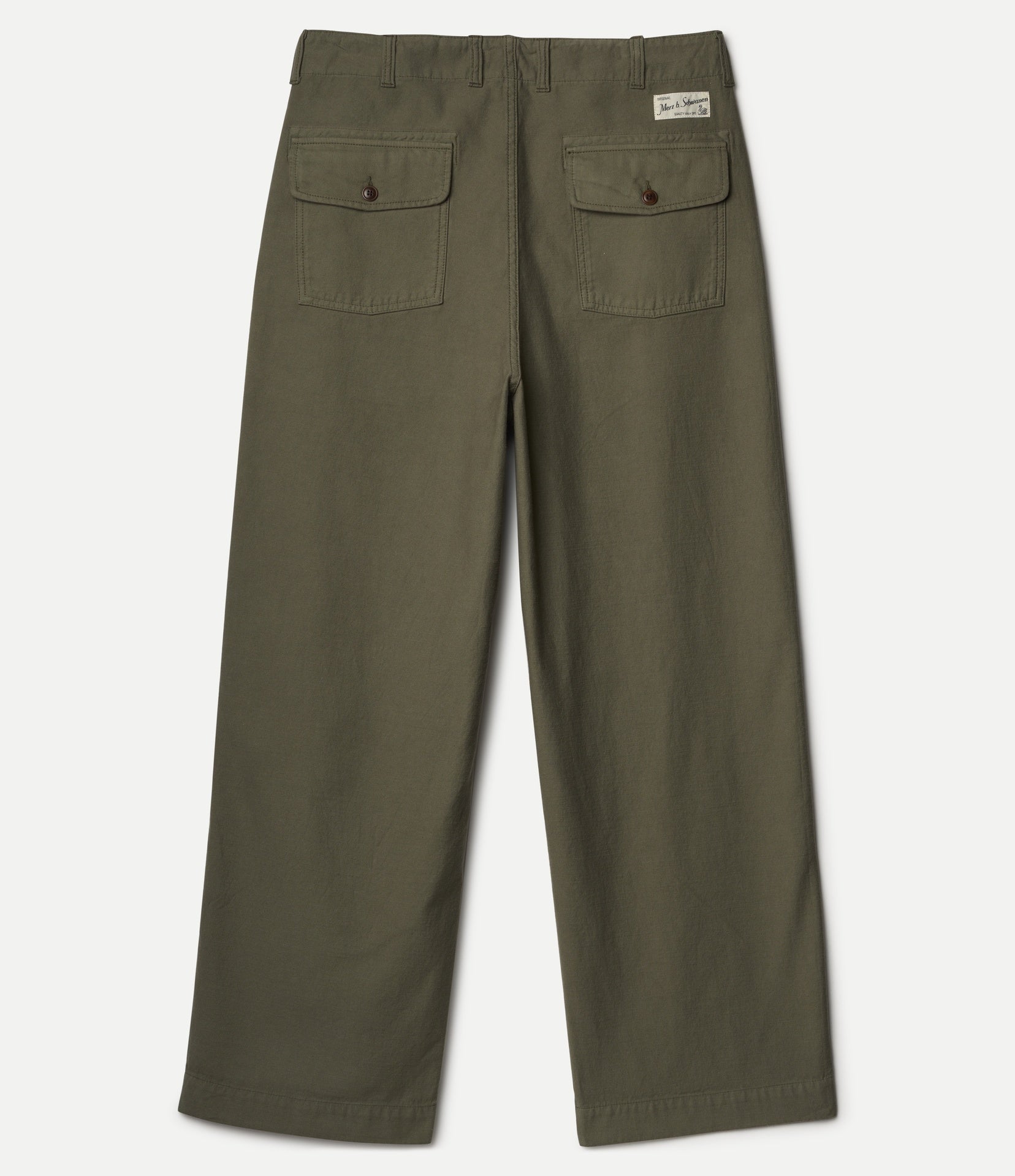 Olive green pants shown from the back, featuring two buttoned flap pockets and a small white Merz b. Schwanen brand label near the top right waistband, set against a light gray background.