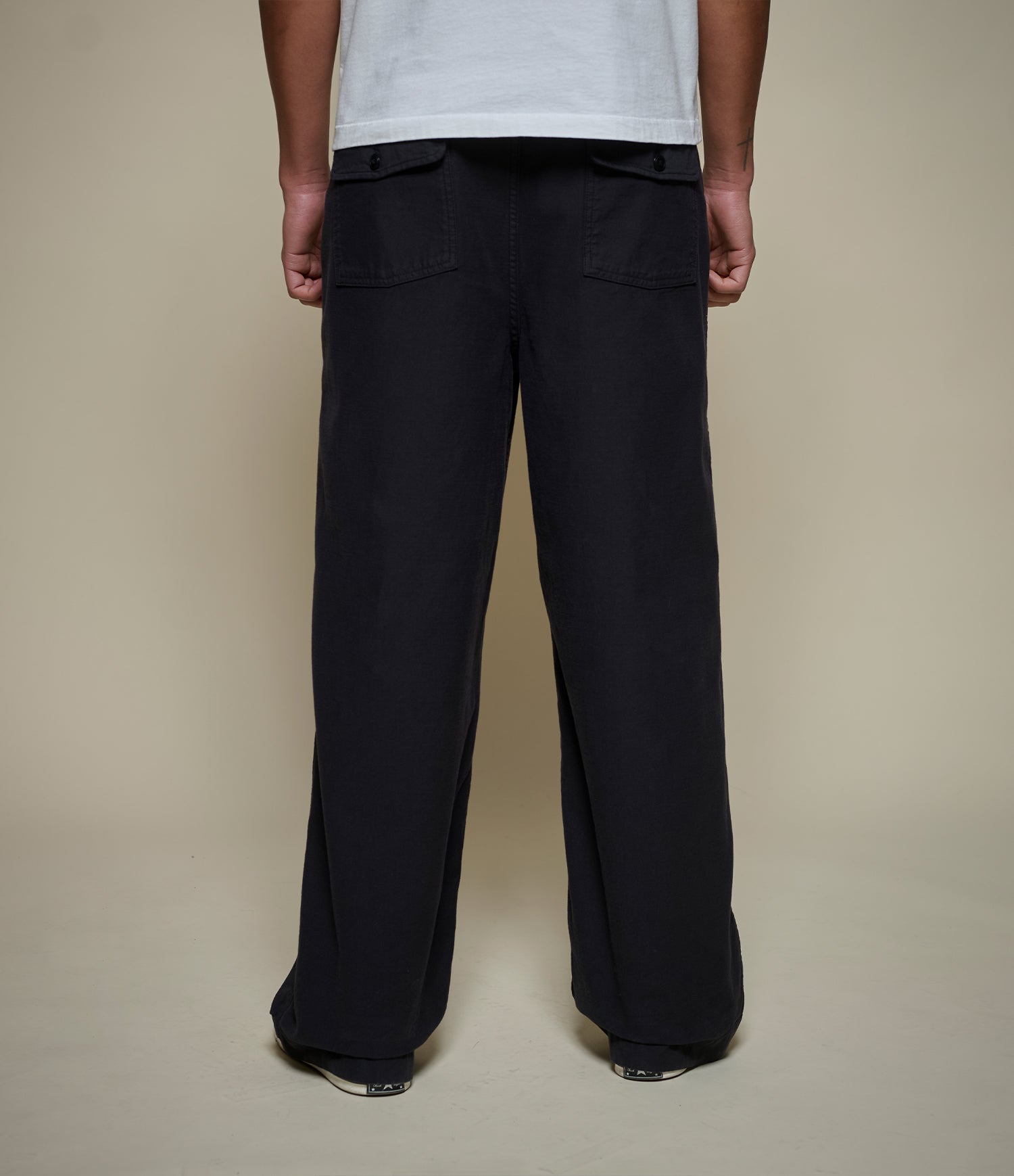 A person shown from the back wearing loose black wide-leg pants and a white T-shirt against a plain beige studio background.