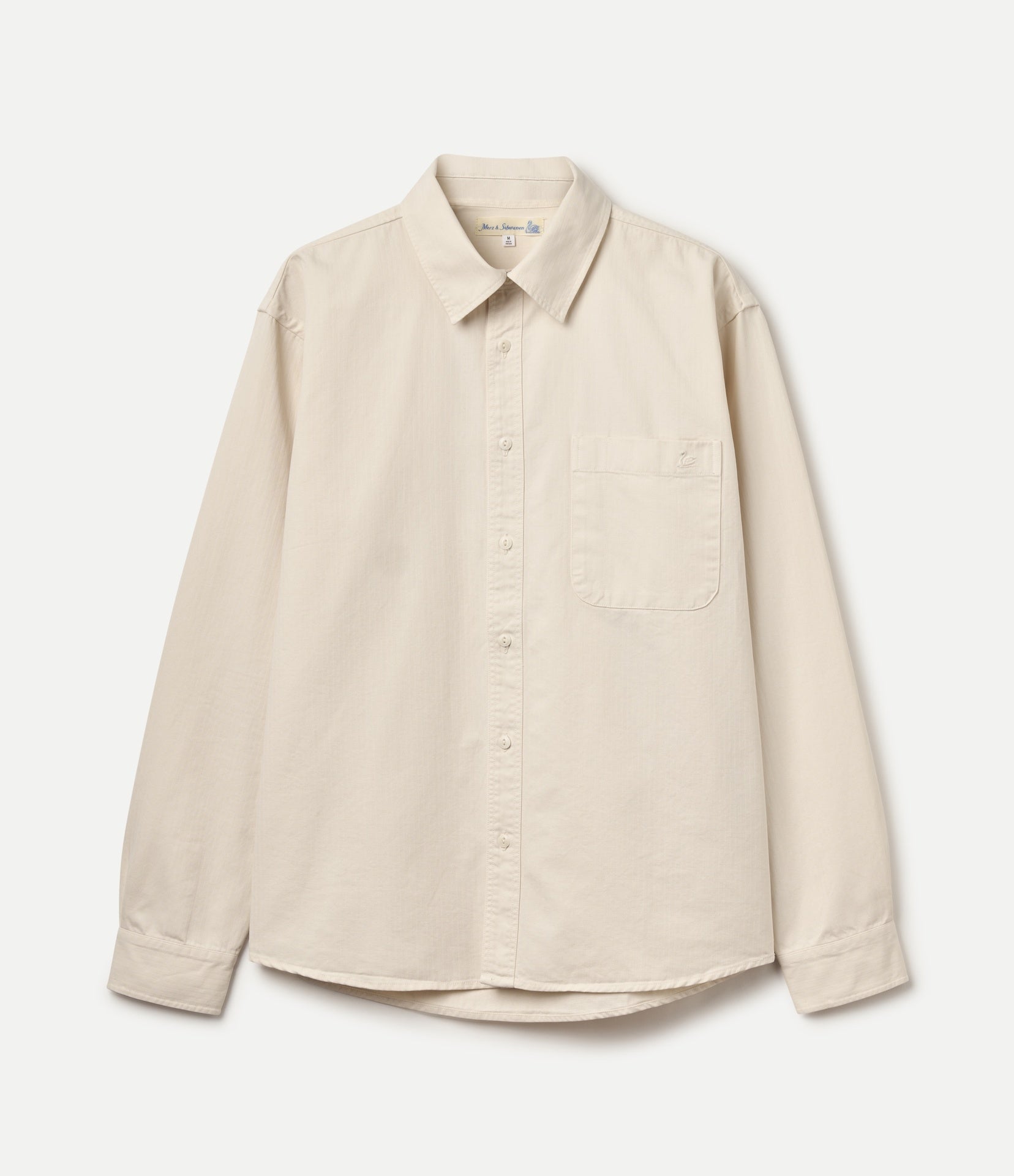 A light beige long-sleeve button-up herringbone twill shirt with a classic collar, single chest pocket, and button cuffs, shown flat against a light off-white background.