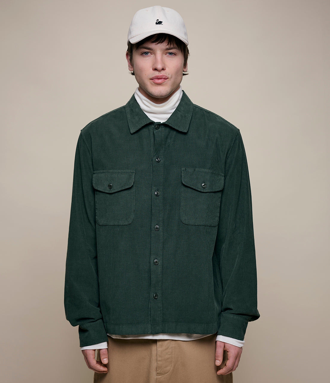 Man wearing a green corduroy shirt with two front pockets on a beige background