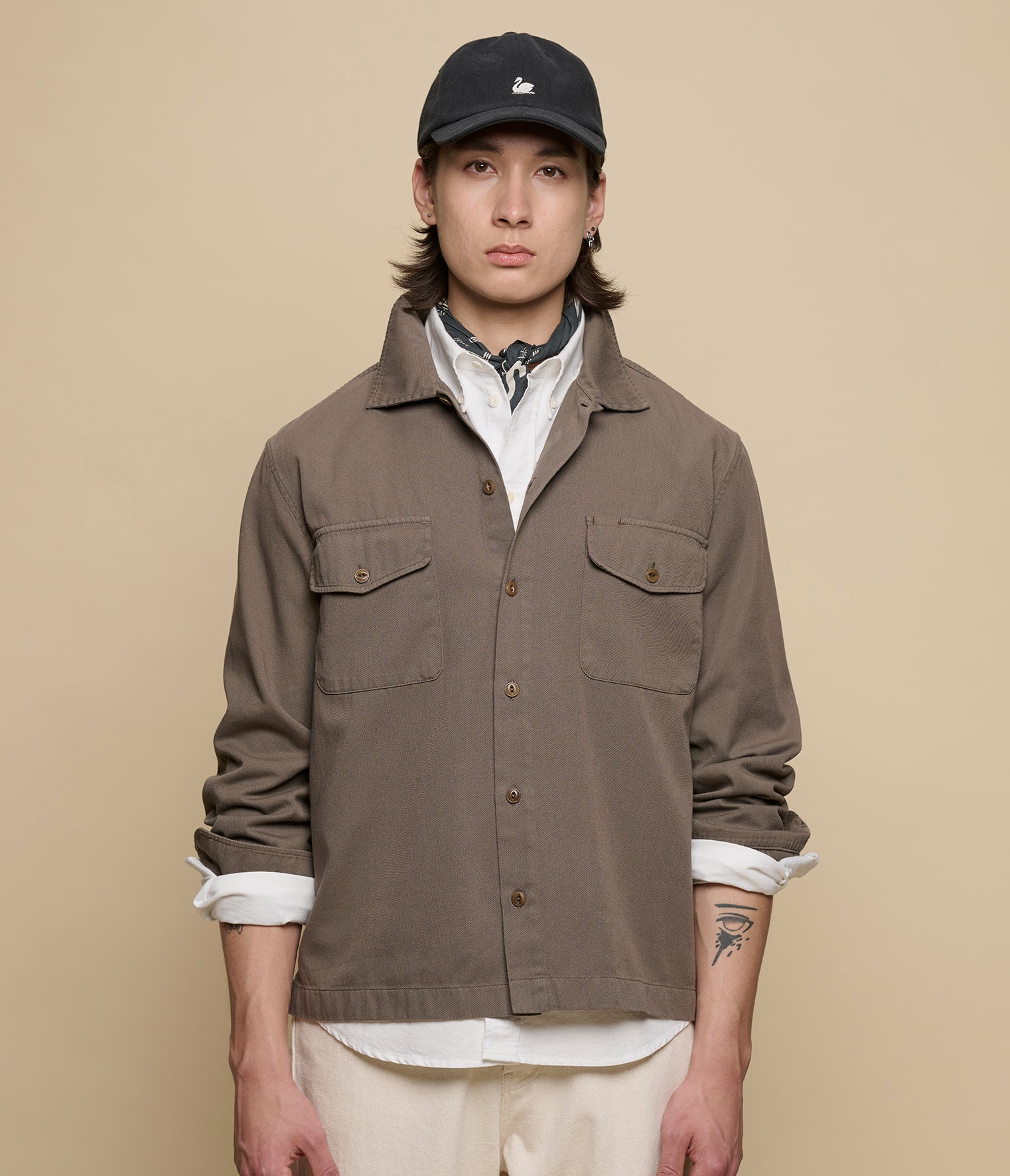Person wearing a brown jacket and black cap on a beige background