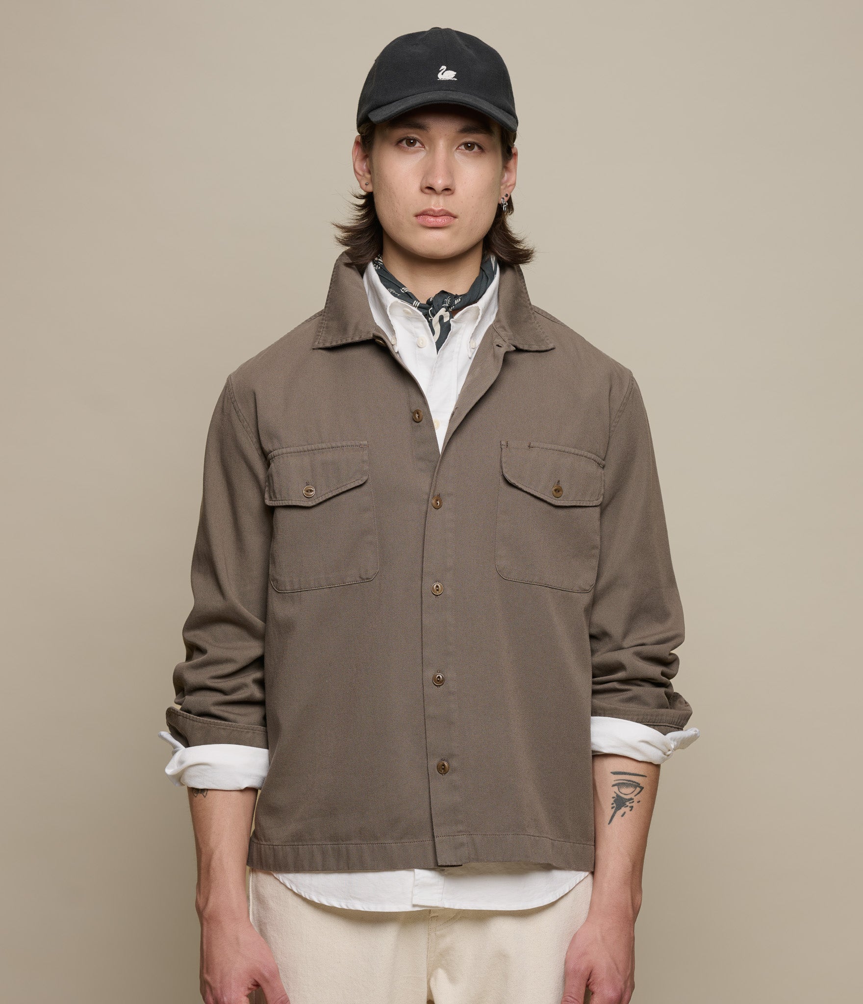 Person wearing a brown jacket and black cap on a beige background
