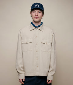 Person wearing a beige jacket and blue cap with 'MbS' logo on a beige background