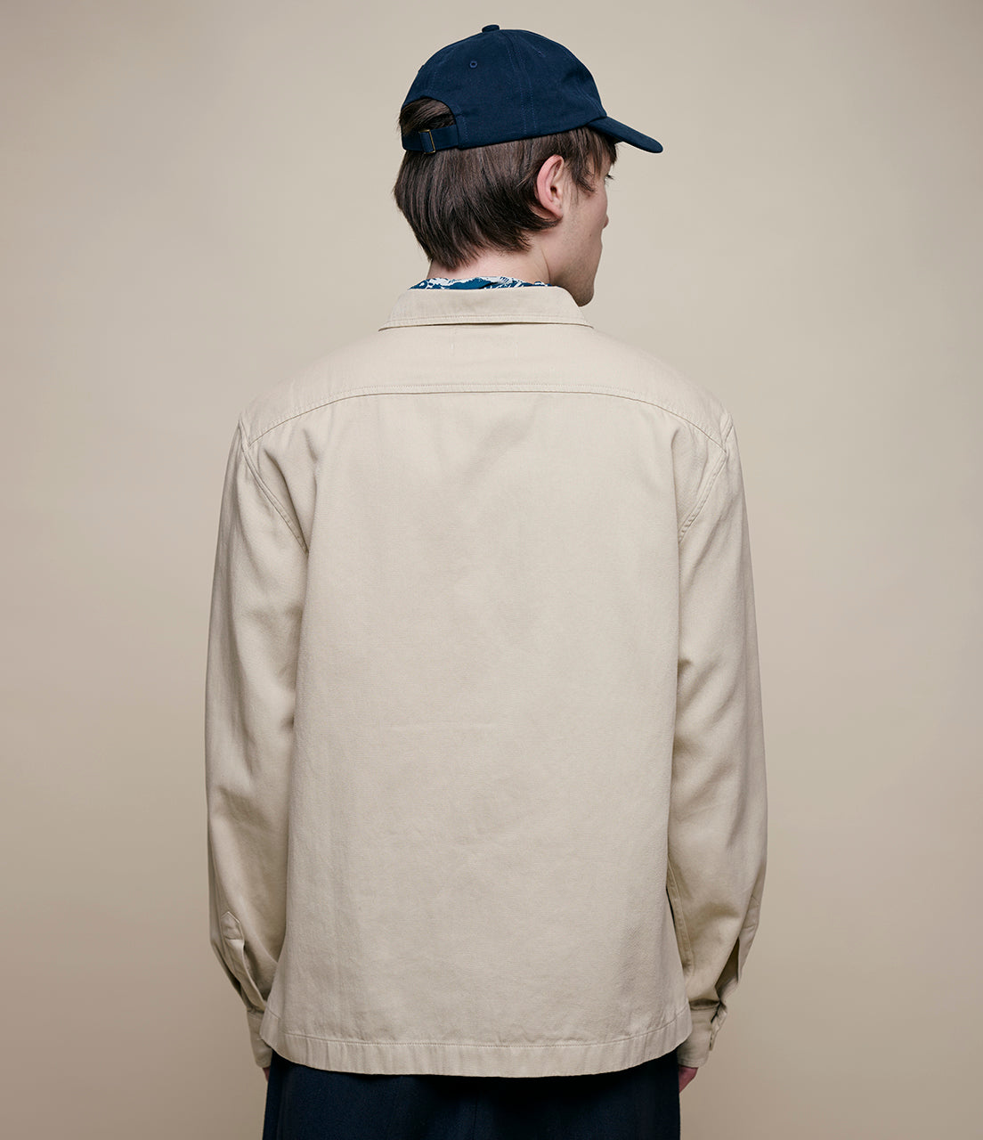 Person wearing a beige jacket and navy cap on a plain background