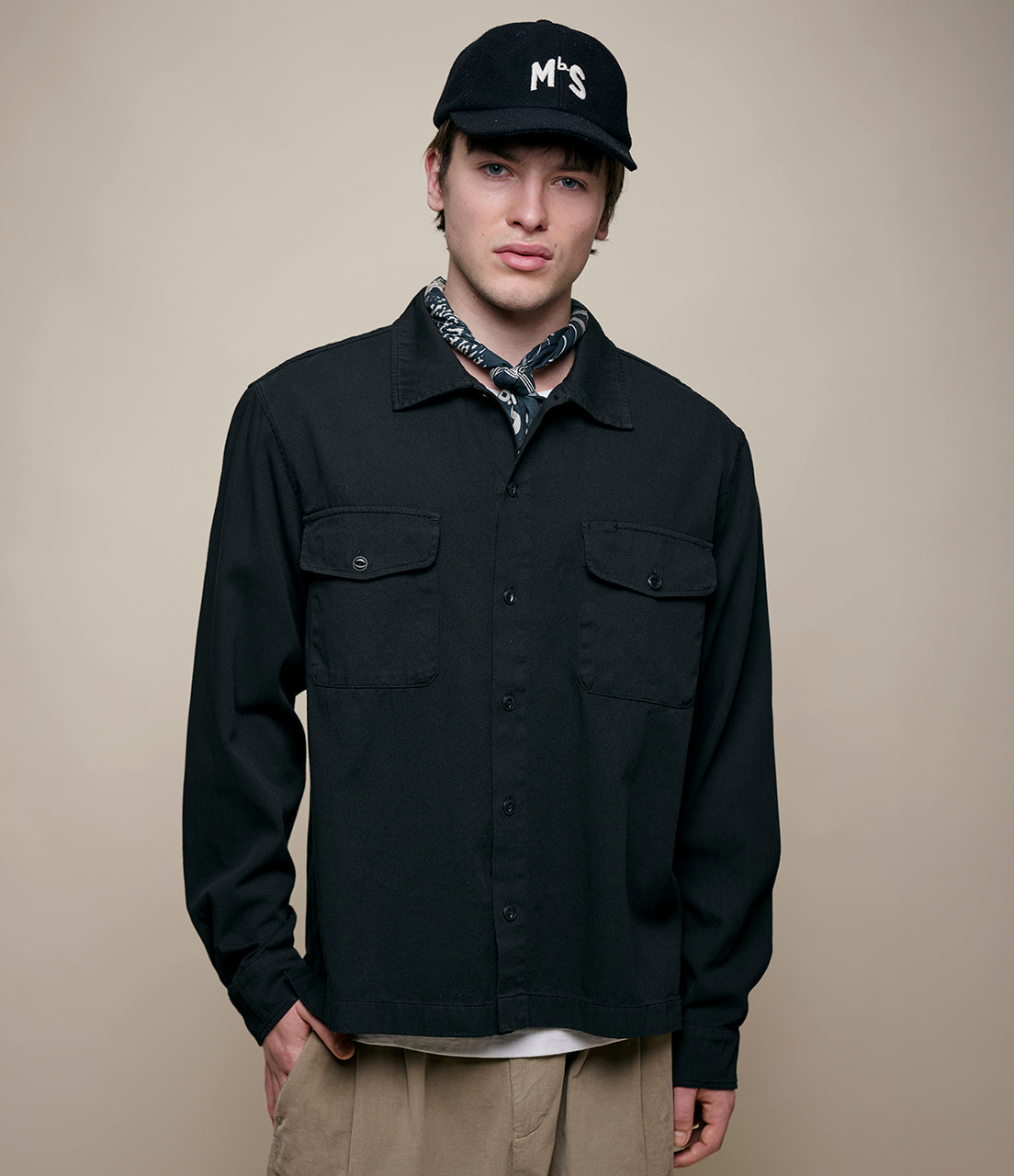 Man wearing a black jacket and cap with a beige background