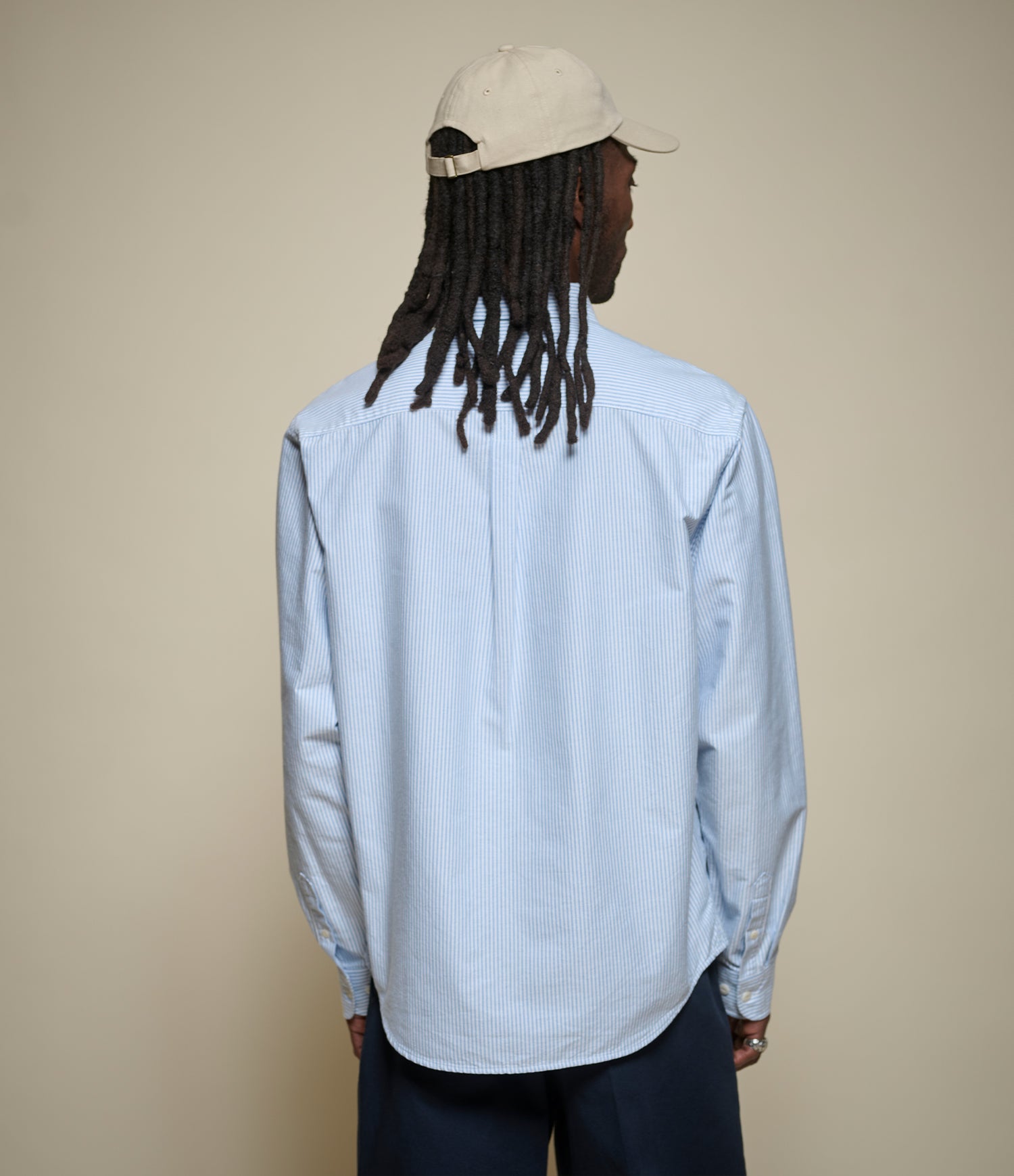 Person wearing a light blue striped shirt and beige cap from behind on a beige background