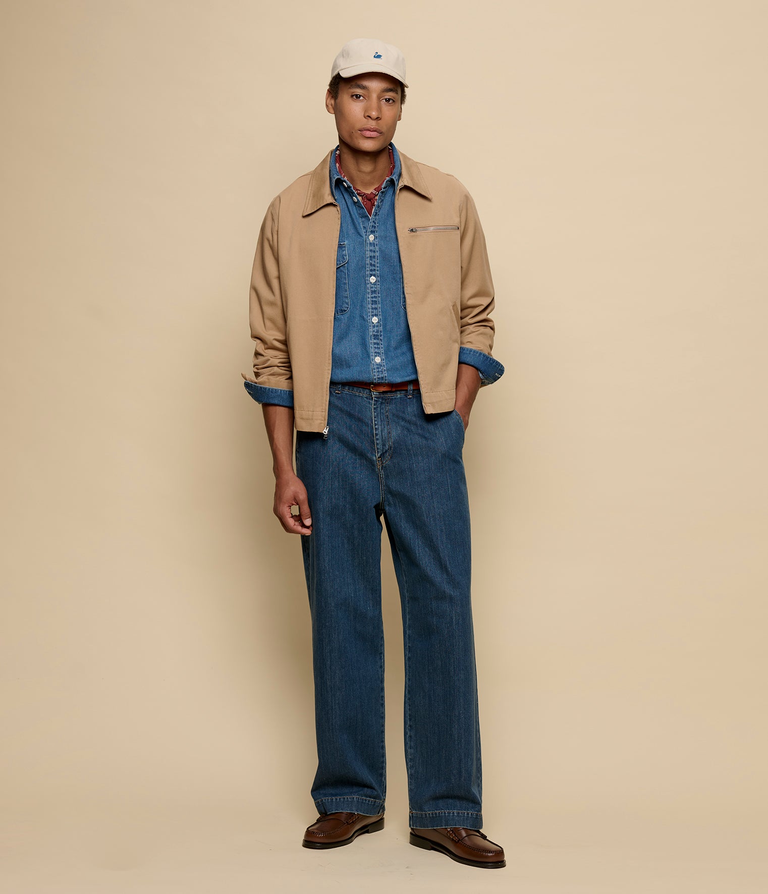Man wearing a beige jacket, blue shirt, and jeans on a beige background