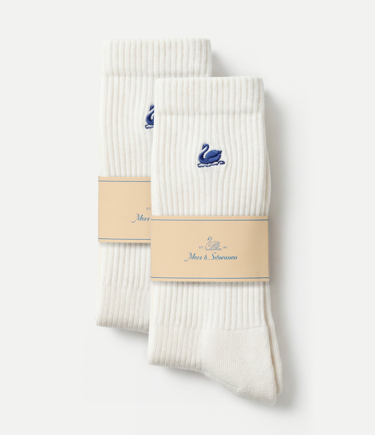Two pairs of white ribbed crew socks with a small blue swan logo, wrapped in beige paper bands, set against a light gray background.