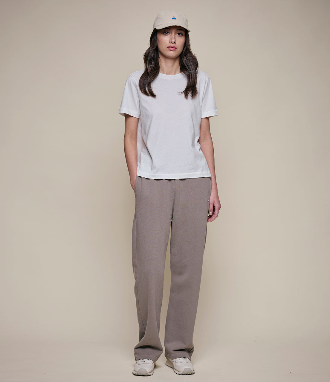 Person wearing a white t-shirt, beige pants, and a cap on a plain background