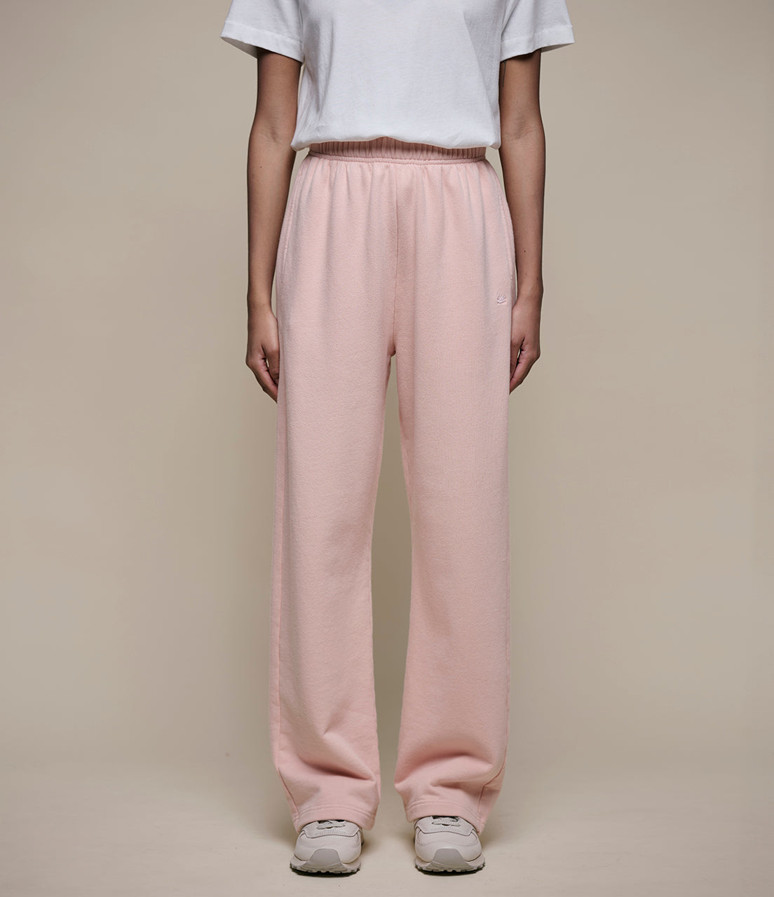 Person wearing light pink pants and a white shirt on a beige background