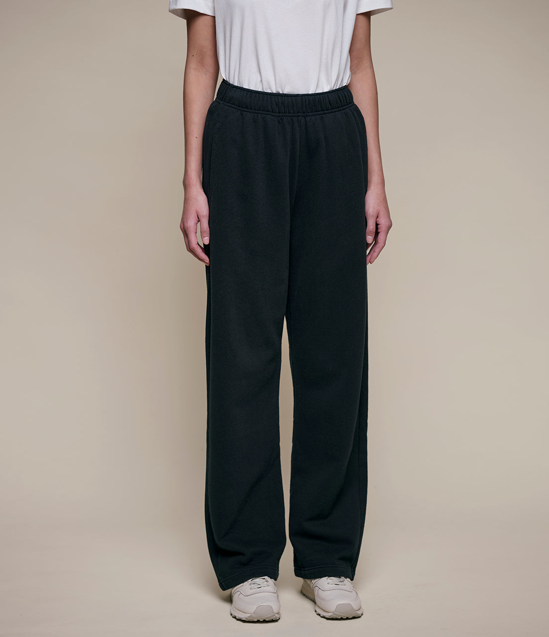 Person wearing black pants and a white shirt on a beige background