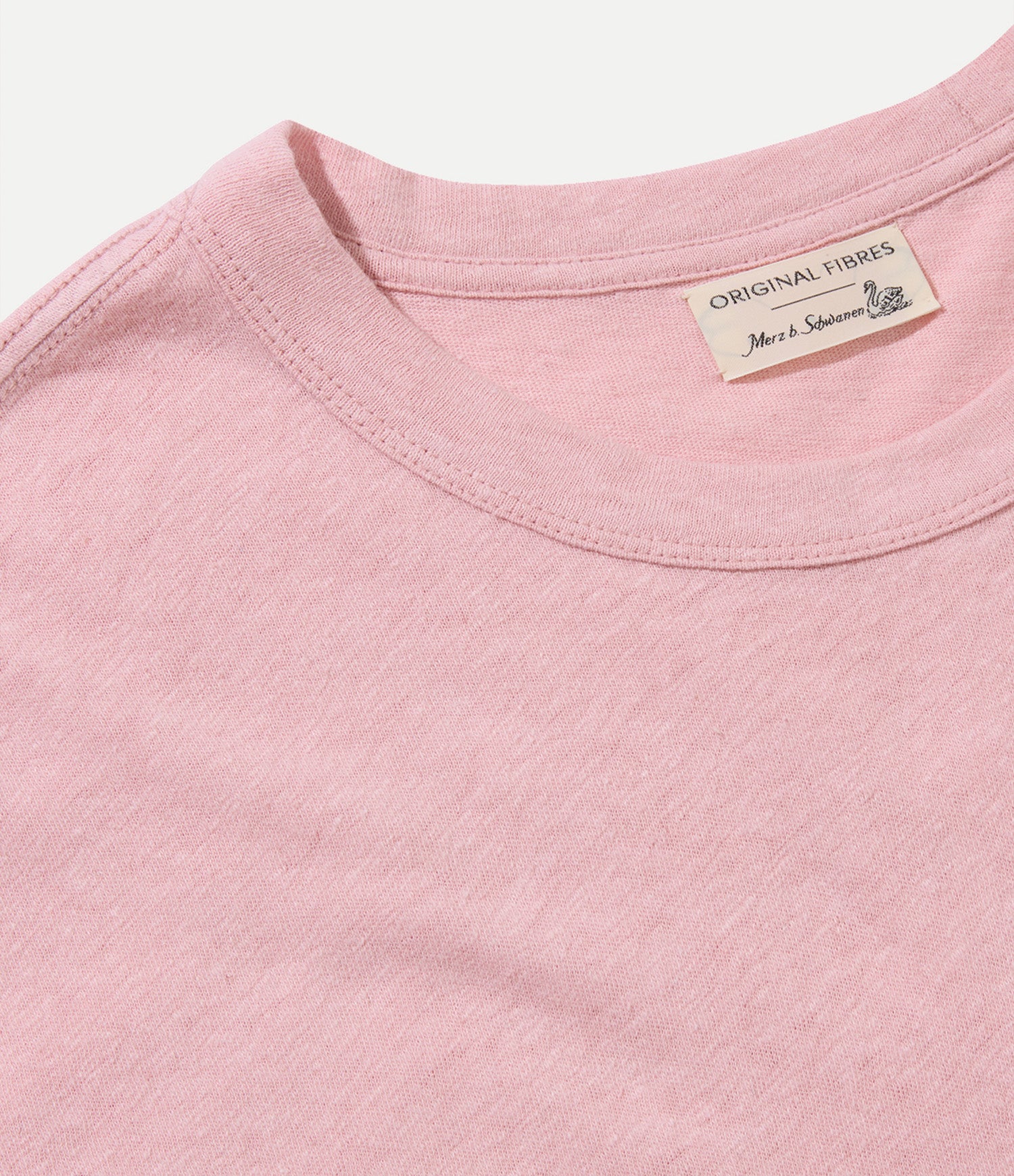 Close-up of a pink shirt with a collaborative Original Fibres x Merz b. Schwanen label on a white background