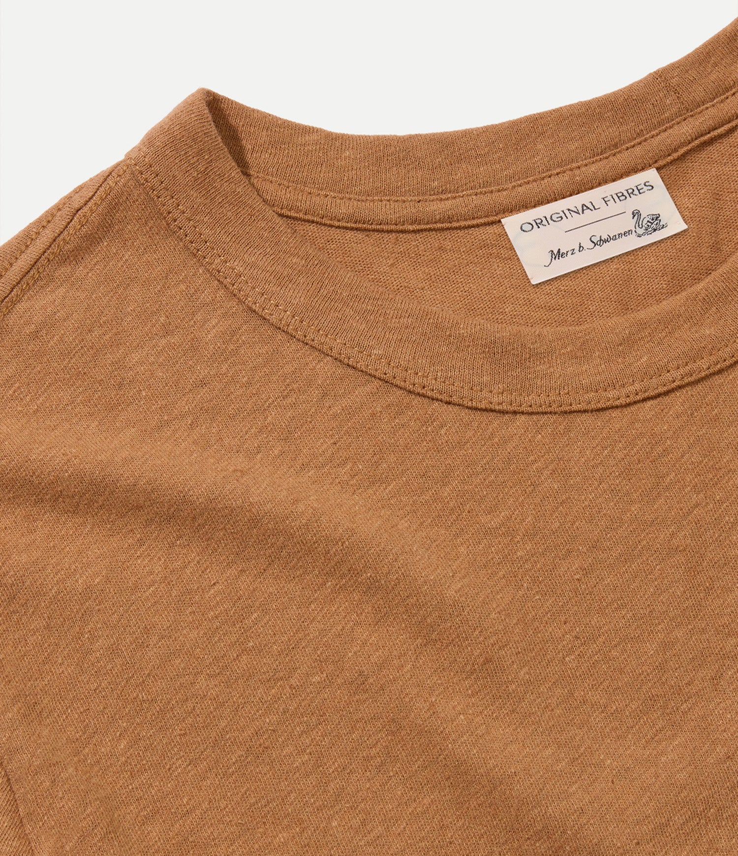 Close-up of a brown shirt with a collaborative Original Fibres x Merz b. Schwanen label on a white background