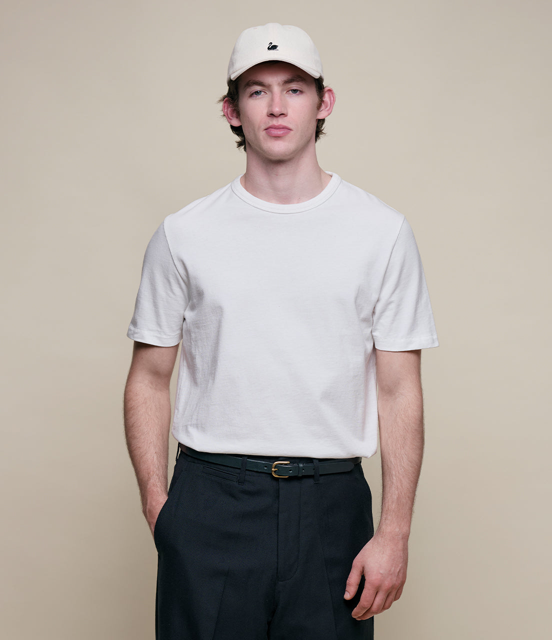 Man wearing white classic cotton jersey T-shirt, beige cap and dark navy pants
