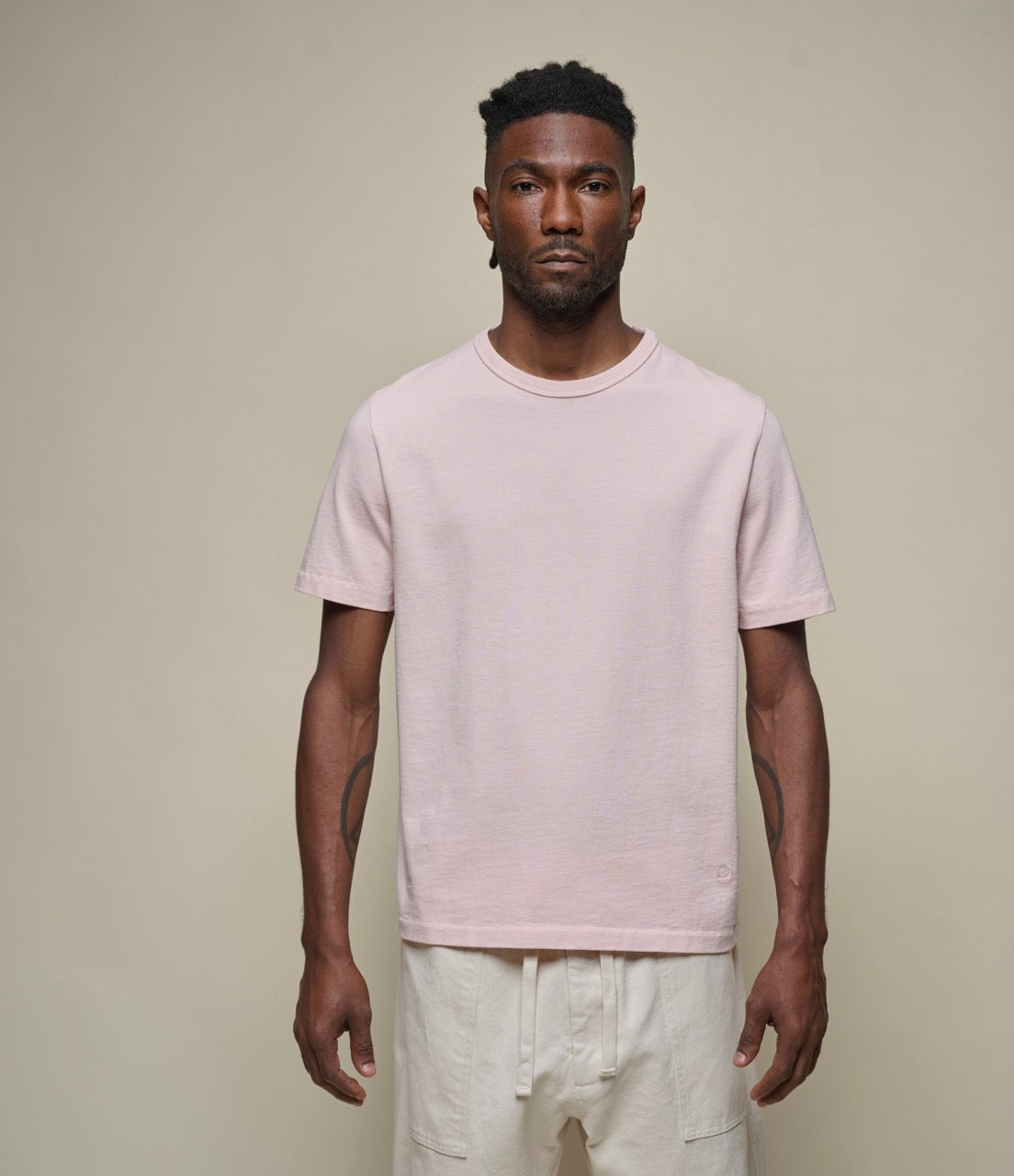 A person wearing a pink, short-sleeved, round-neck T-shirt with side seams, made from organic cotton.
