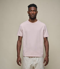 Man wearing a light pink t-shirt and white pants against a beige background