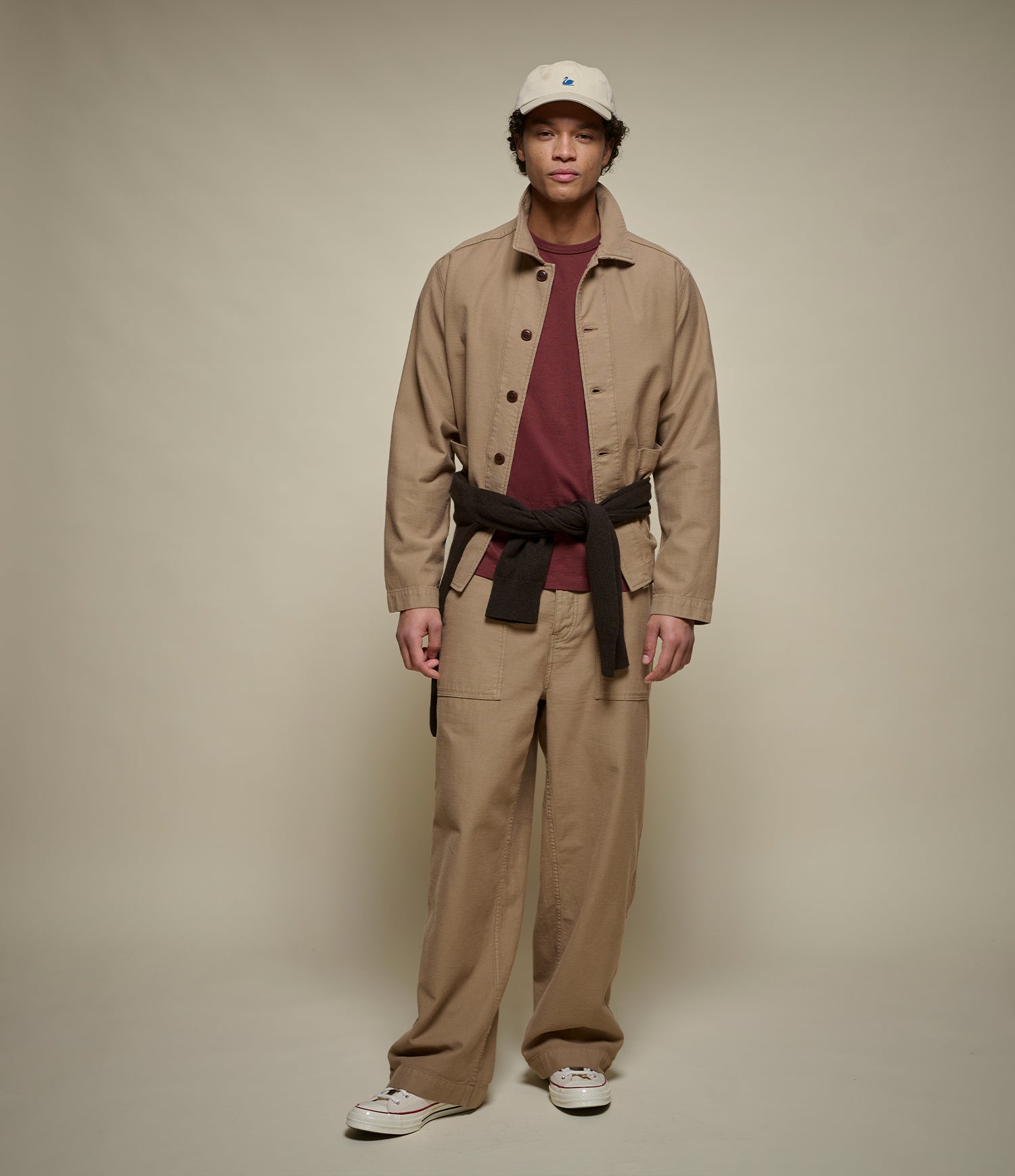 Man wearing a beige cropped jacket over a maroon crew-neck T-shirt and beige fatigue pants.