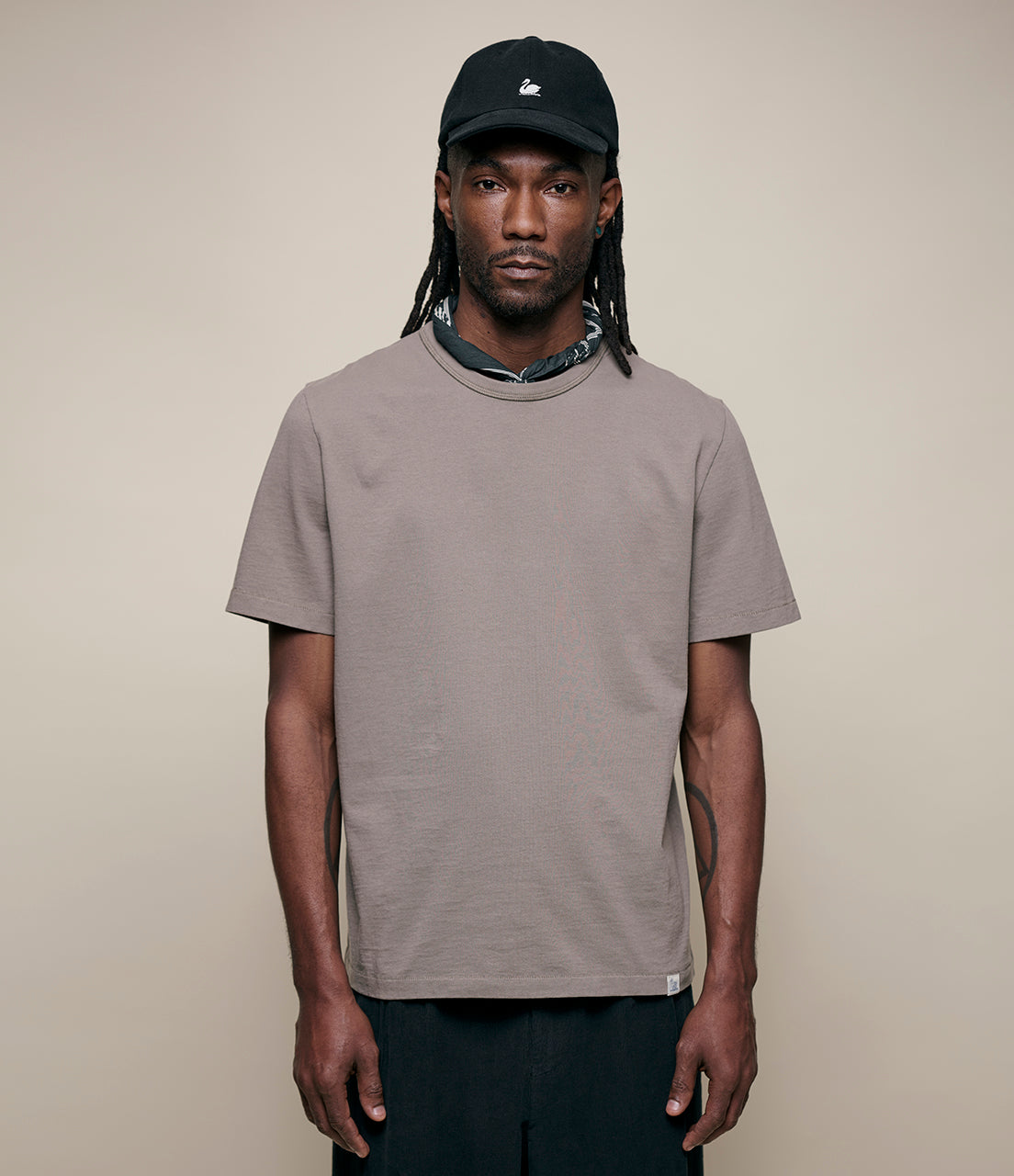 Man wearing a grain t-shirt and black cap against a beige background