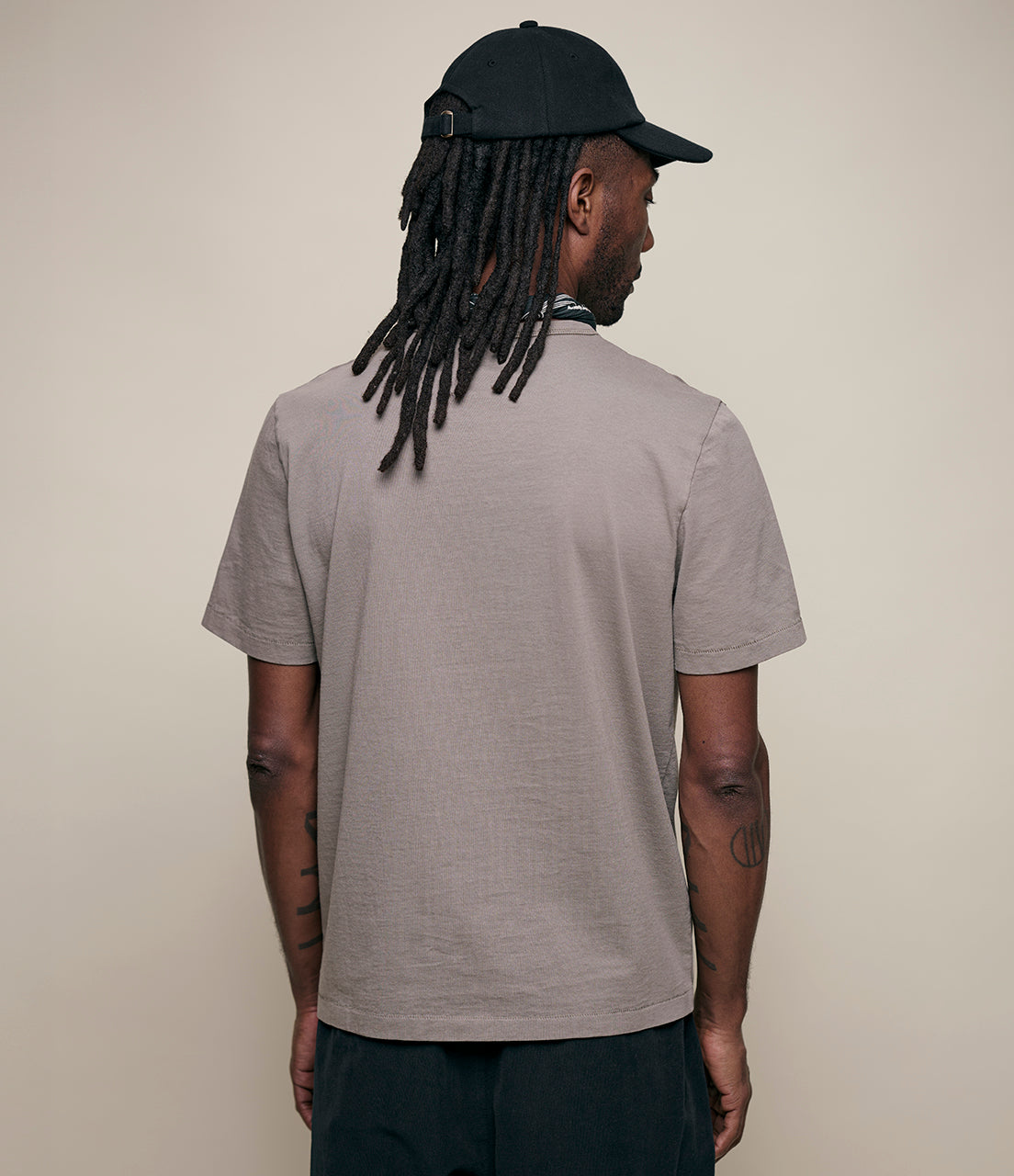 Man wearing a gray t-shirt and black cap from behind on a beige background