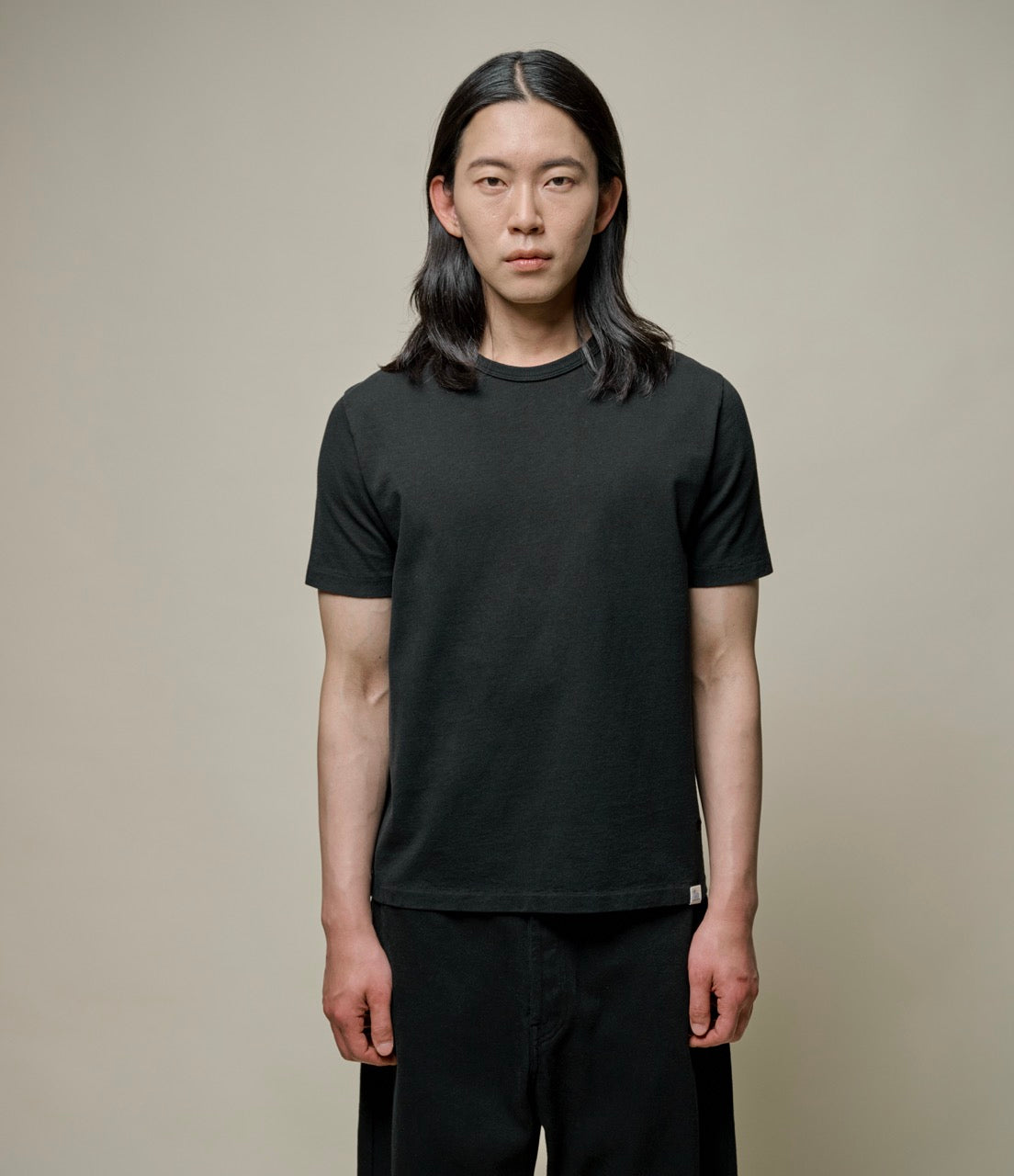 A person wearing a black crew neck T-shirt and black pants, standing against a plain background.